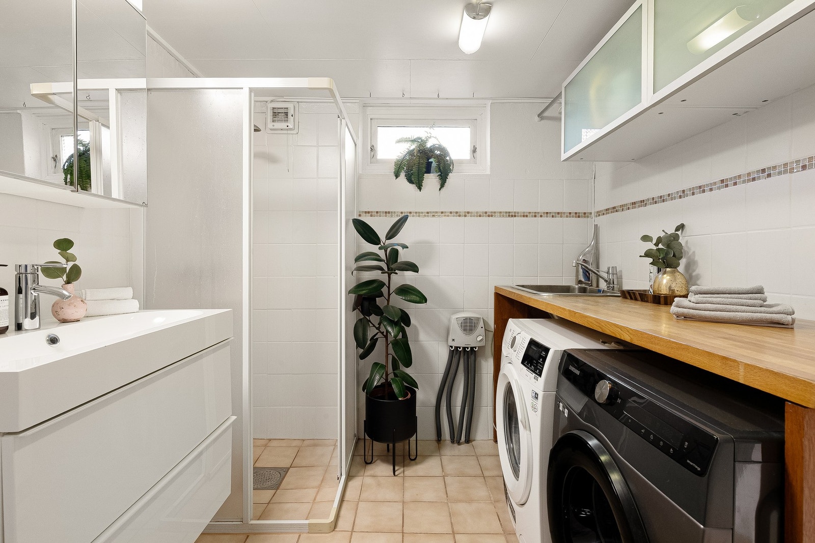 Bad med en praktisk løsning! Her finnes også en egen sone for vaskemaskin og tørketrommel, med benkeplate, vask og veggskap med klesstang. Galleribilde