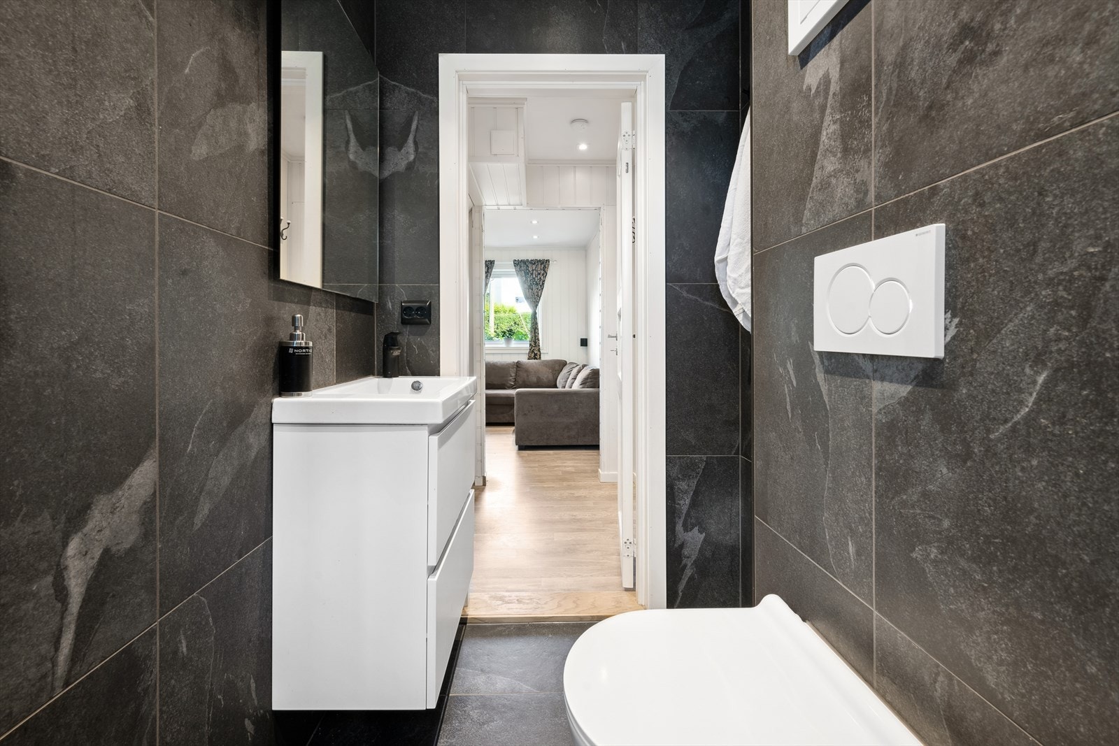 Innredningen har slette fronter og en heldekkende servant med ett-greps blandebatteri og plastavløp. Badet har også et vegghengt toalett. Galleribilde