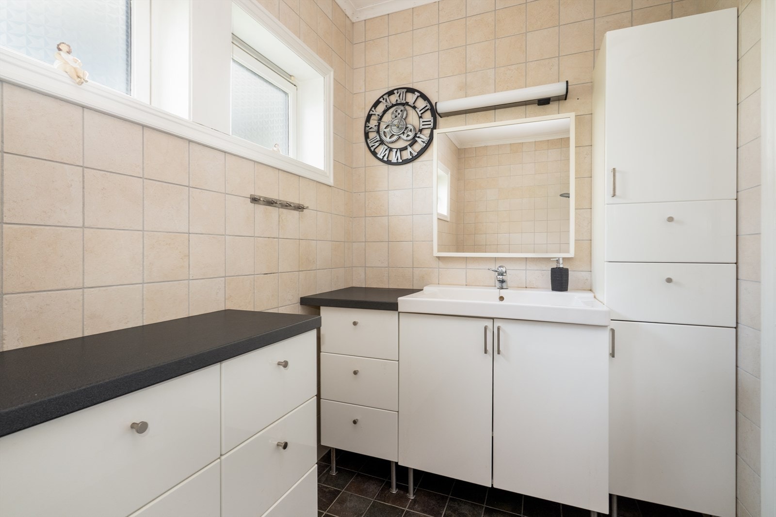 Badet er innredet med badekar med glassvegg, toalett og servantinnredning med skap, skuffer, speil og overlys. Galleribilde