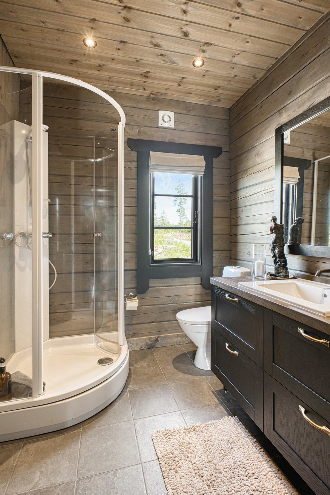 Grå gulvfliser kombineres med tømmerveggene, og begge badene har toalett, dusjkabinett og varmekabler Galleribilde