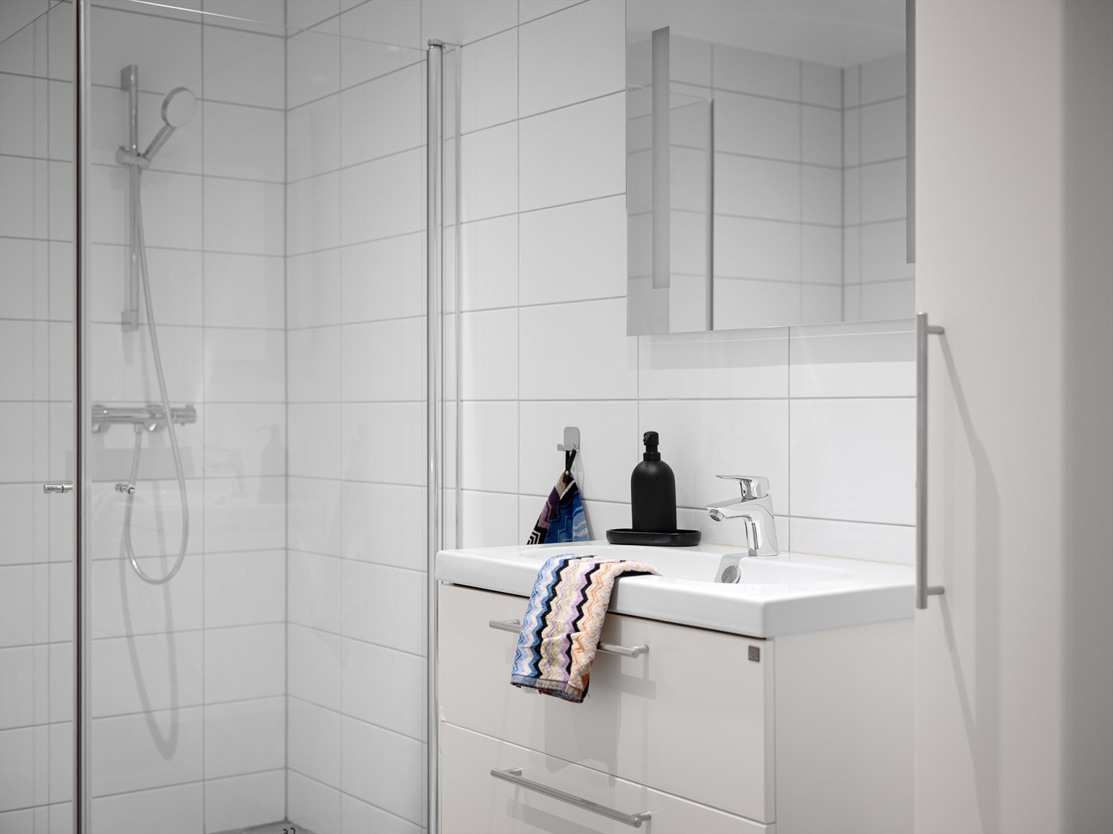 Flislagt bad med vegghengt toalett, dusjnisje og vask i skap Galleribilde