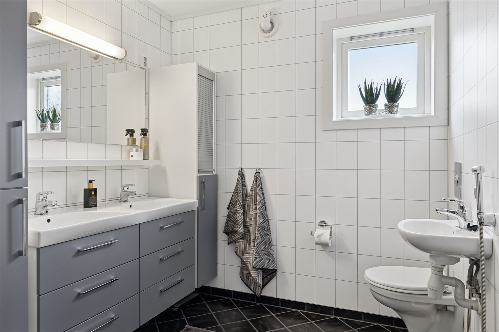 Badet er ellers utstyrt med dusjkabinett fra 2024, vegghengt toalett, servant og baderomsinnredning med to nedfelte servanter. Avtrekk via mekanisk vifte. Galleribilde