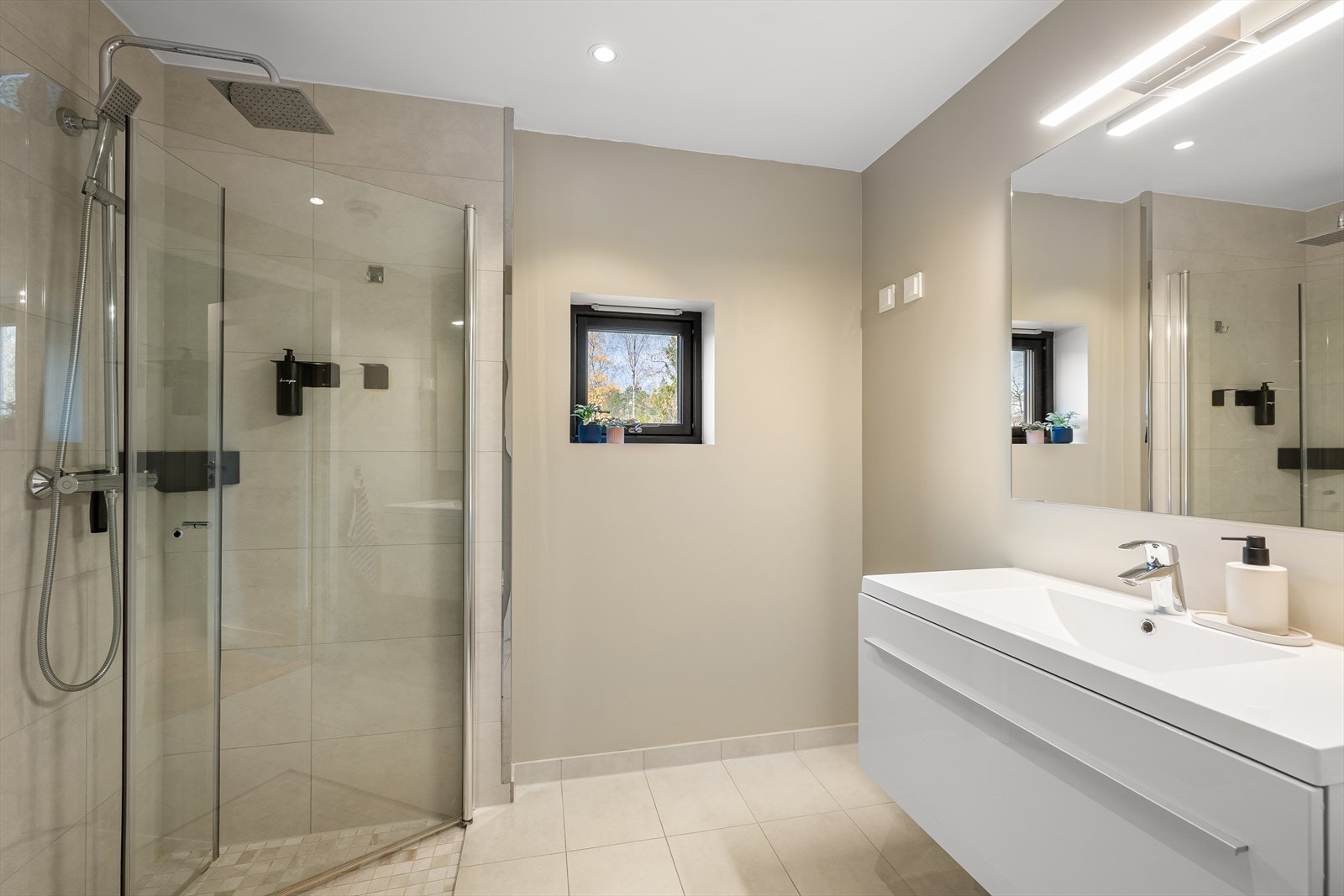 Badene har dusj med innfellbare dører i herdet glass og veggfestet toalett og servant Galleribilde