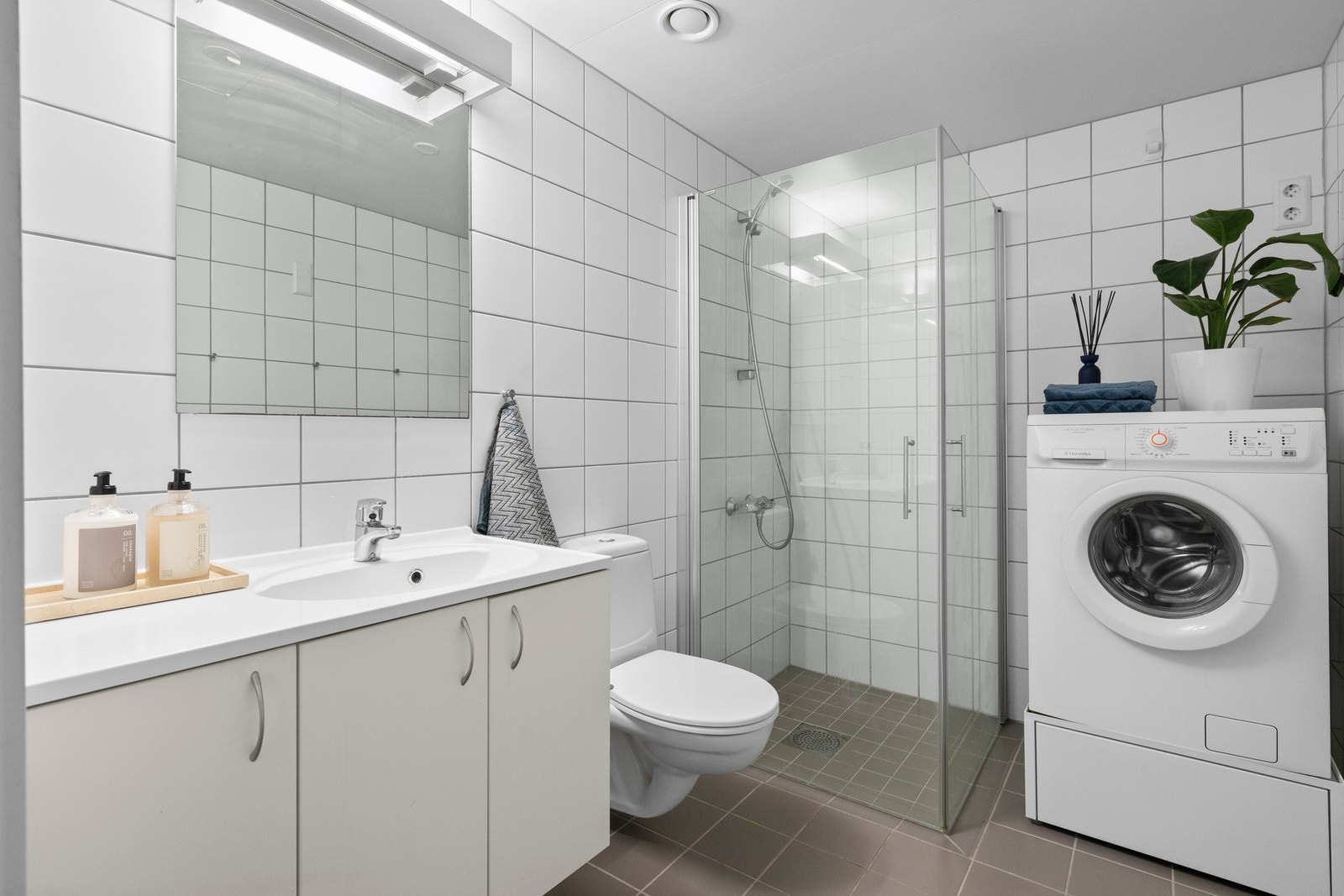Lekkert og praktisk bad med fliser på både gulv og vegger i et tidløst uttrykk. Den innfellbare dusjløsningen og vegghengte toalettet bidrar til en luftig og moderne følelse, mens innredningen med nedfelt servant gir god funksjonalitet. Opplegg for vaskem Galleribilde