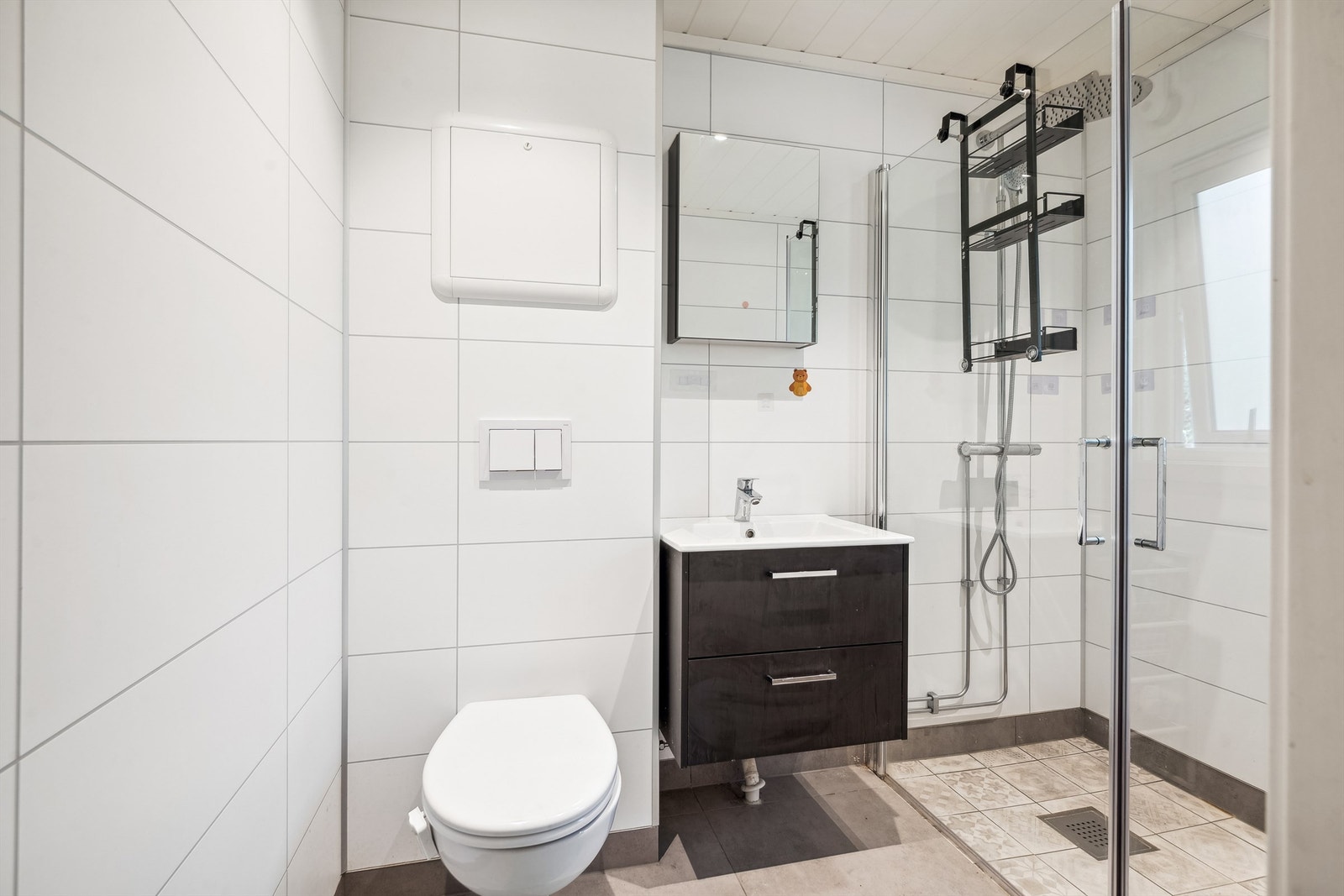 Pent baderom fra 2020. Vegger med baderomsplater og gulvet er flislagt med varmekabler. Vegghengt innredning med nedfelt servant og speilskap og dusjhjørne. Galleribilde