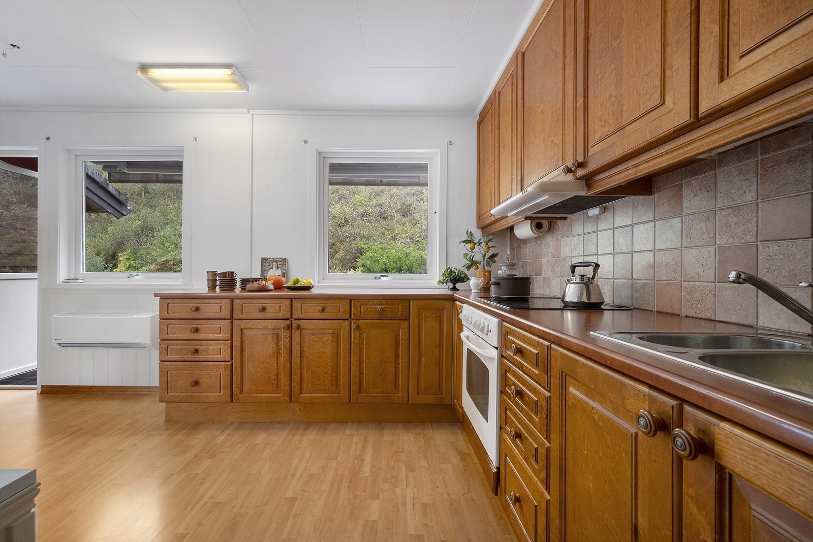 Kjøkkenet har innredning med profilerte fronter av eik og laminert benkeplate. Her er det fliser på vegg ved benkeplaten med belysning under overskap. Galleribilde