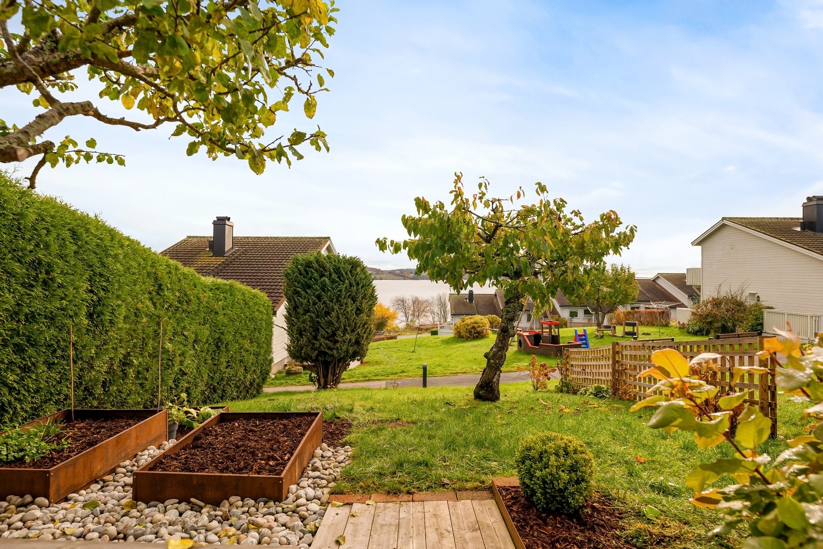 går det videre ut i den pent opparbeidede hagen med plen, beplantning og skjermende hekk Galleribilde