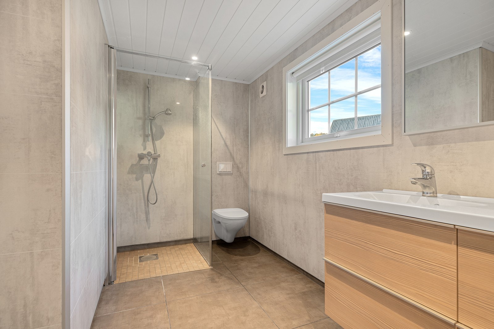 Smakfullt bad med flislagt gulv med vannbåren varme. Badet er innredet med servant, dusjhjørne med innfellbare dører og vegghengt toalett Galleribilde