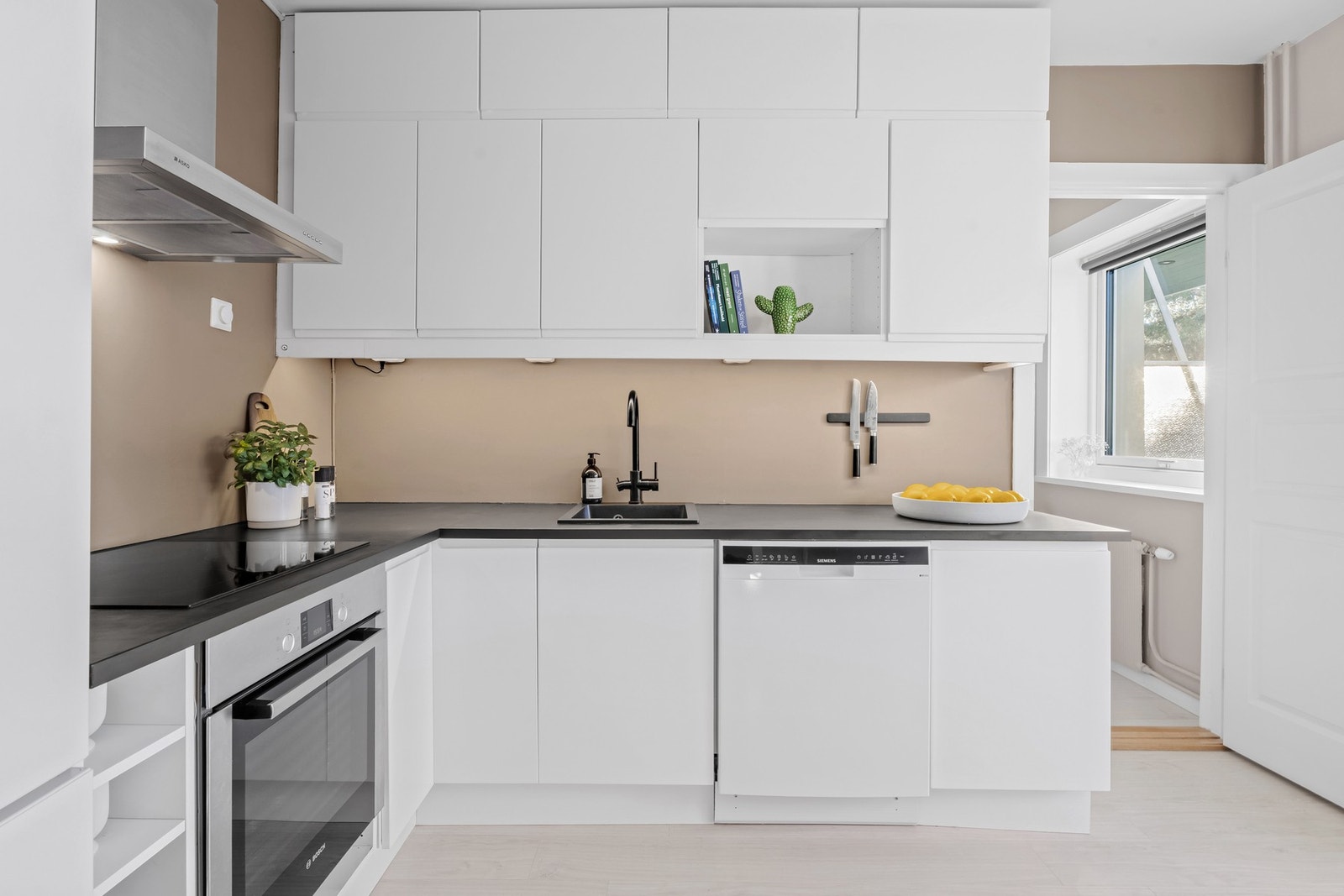 Kjøkkenet har en takhøy innredning med slette, hvite fronter og sort laminat benkeplate Galleribilde