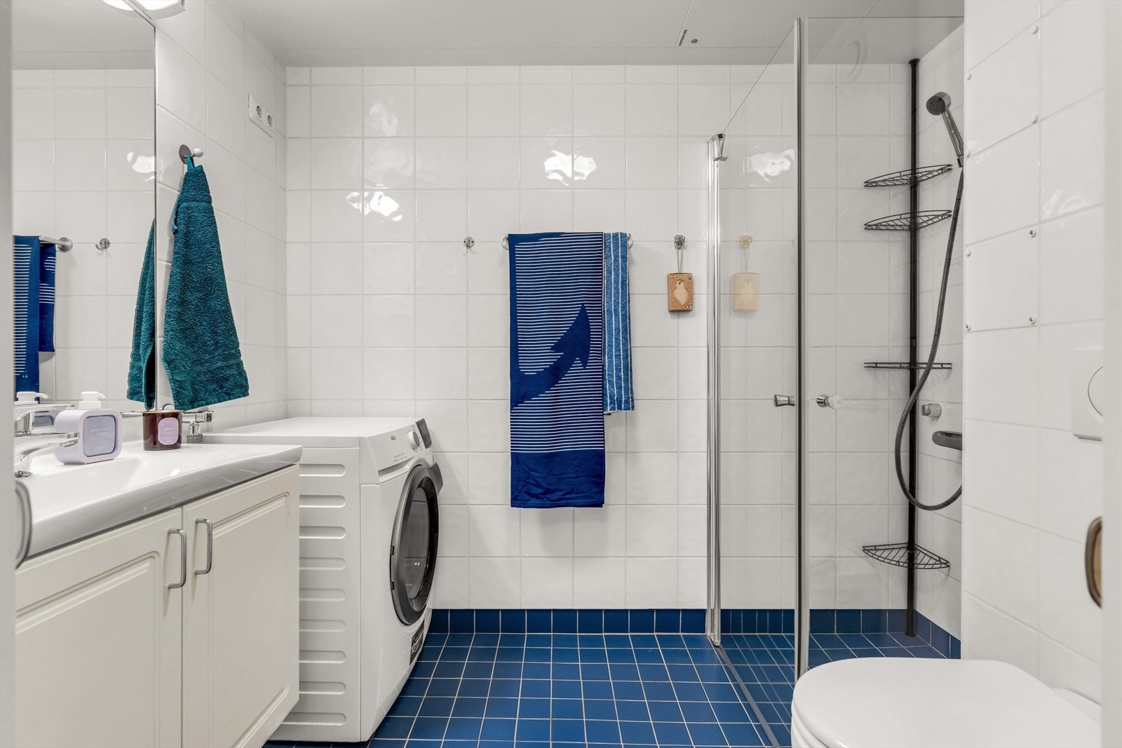 Flislagt baderom med med lyse veggfliser og blå gulvfliser. Galleribilde