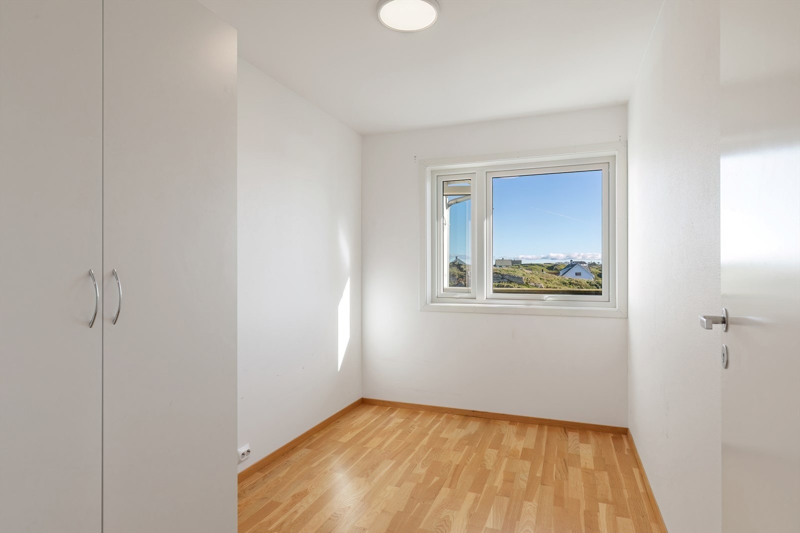 Lyst rom med parkettgulv og innebygd garderobe gir praktisk oppbevaring. Vindusplassering gir utsyn mot grøntområde og naturlig lysinnslipp. Galleribilde