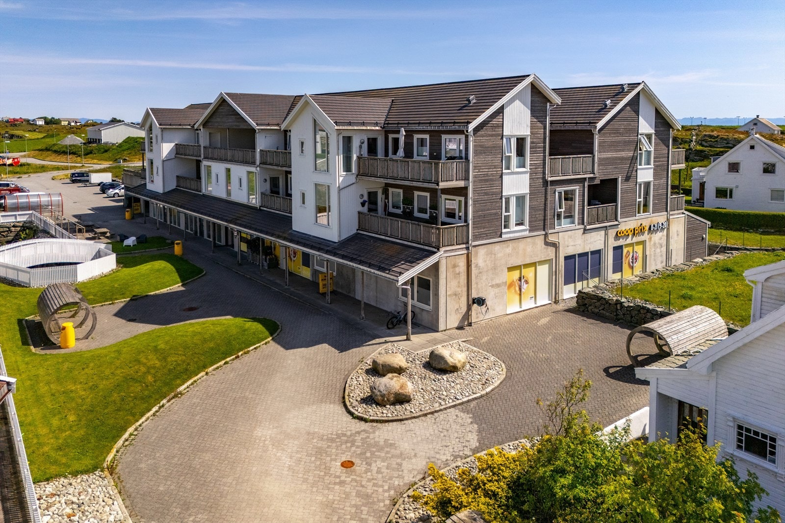 Leilighetsbygget har en moderne fasade med trepanel og store vindusflater, samt en tilknyttet butikk på bakkeplan. Galleribilde