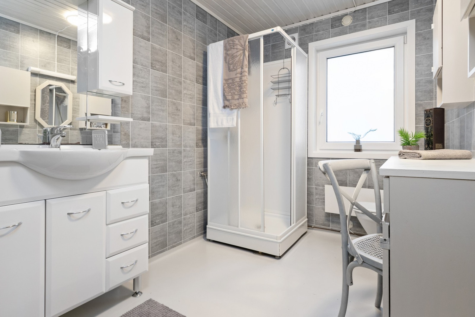 Bad med grå fliser og lyse innredninger - praktisk planlagt med dusjkabinett, servant og oppbevaring. Galleribilde