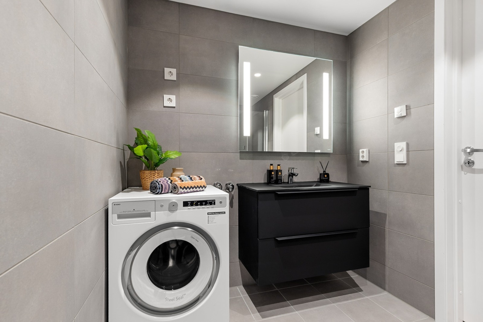 Badet har servant med underskap, speil med LED lys og opplegg for vaskemaskin Galleribilde