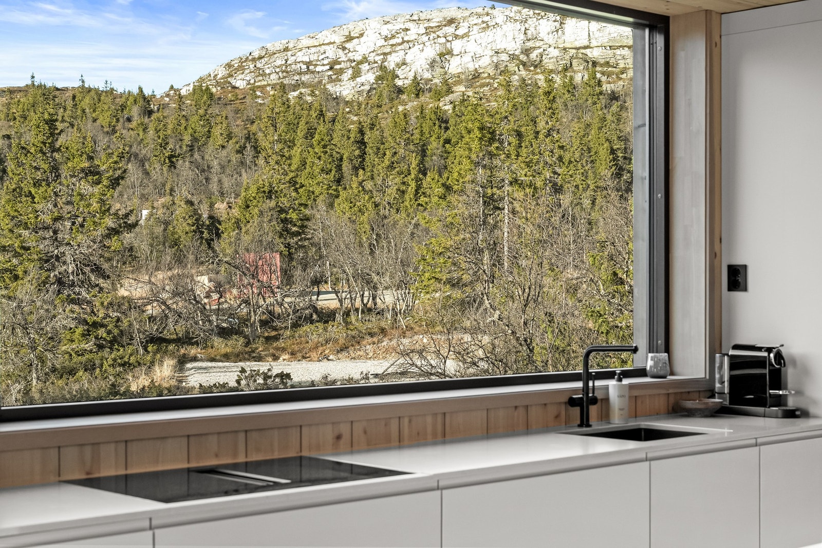 Benkeplate i kompositt fra Caesarstone. Underlimt vaskekum og 80 cm induksjonsplatetopp med benkeventilator. Og lys, masse naturlig lys. Kvitfjelltoppen i bakgrunnen. Galleribilde