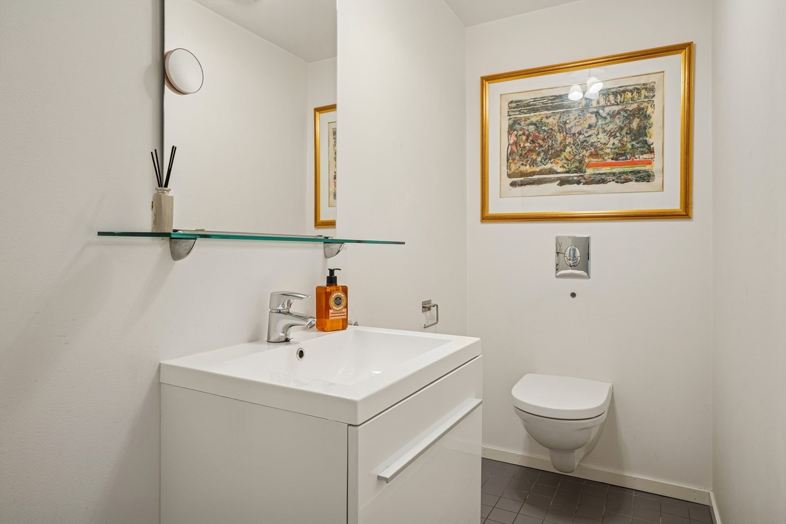 Toalettrommet har fliser på gulv og malte flater på vegger. Rommet er utstyrt med servant med ett-greps blandebatteri og vegghengt toalett. Galleribilde