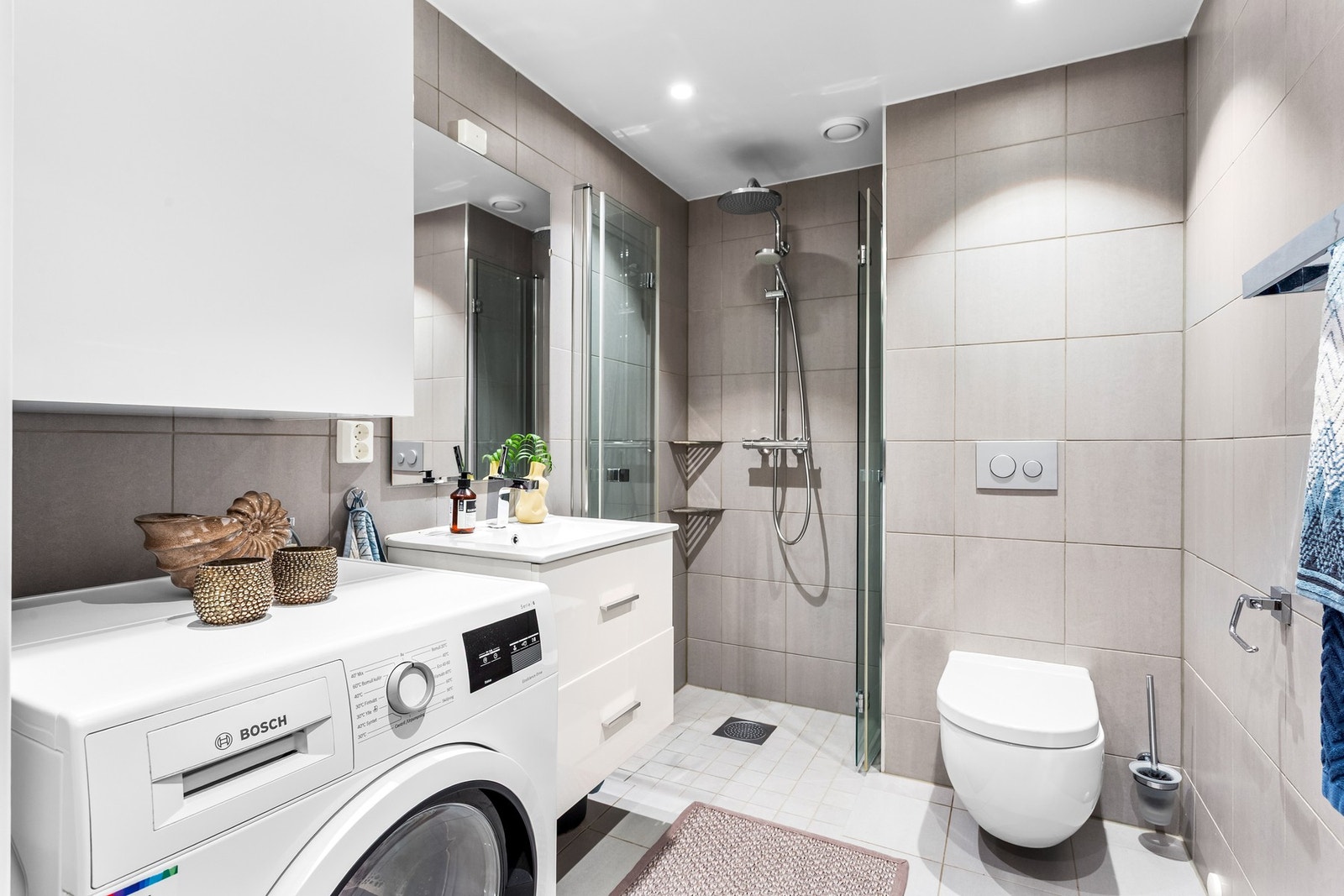 Badet er moderne og pent med fritthengt overskap, vegghengt toalett, dusjsone med to foldedører av glass og opplegg for vaskemaskin. Galleribilde