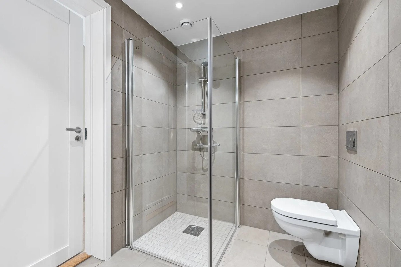 Badet har dusjnisje med glassdører og vegghengt toalett. Galleribilde