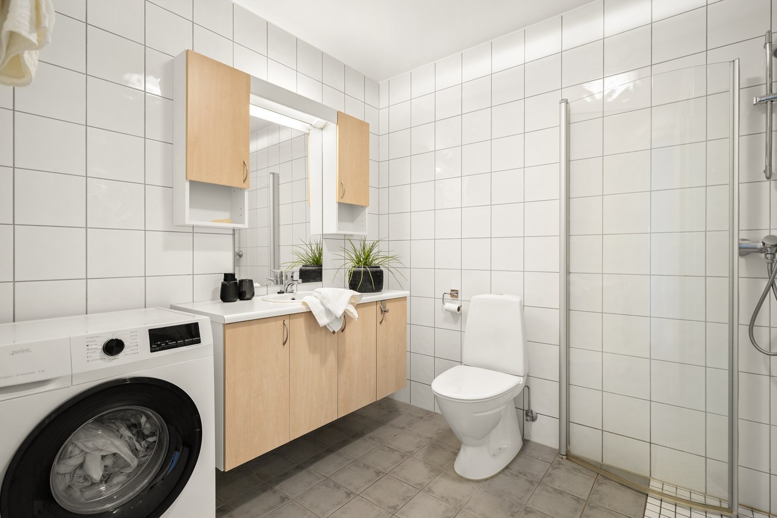 Flislagt bad består av servant med innredning, dusjhjørne med innfellbare dører og gulvklosett. Opplegg for vaskemaskin og tørketrommel. Galleribilde