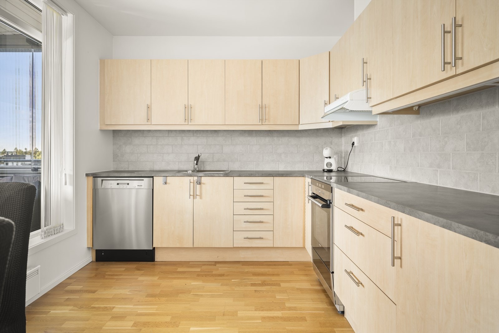 Kjøkkeninnredning med slette laminerte fronter kombinert med laminerte benkeplater. Fliser på vegg i forbindelse med innredningen og lys under overskap. Det er avsatt plass for komfyr og oppvaskmaskin og plass til frittstående kjøleskap. Galleribilde