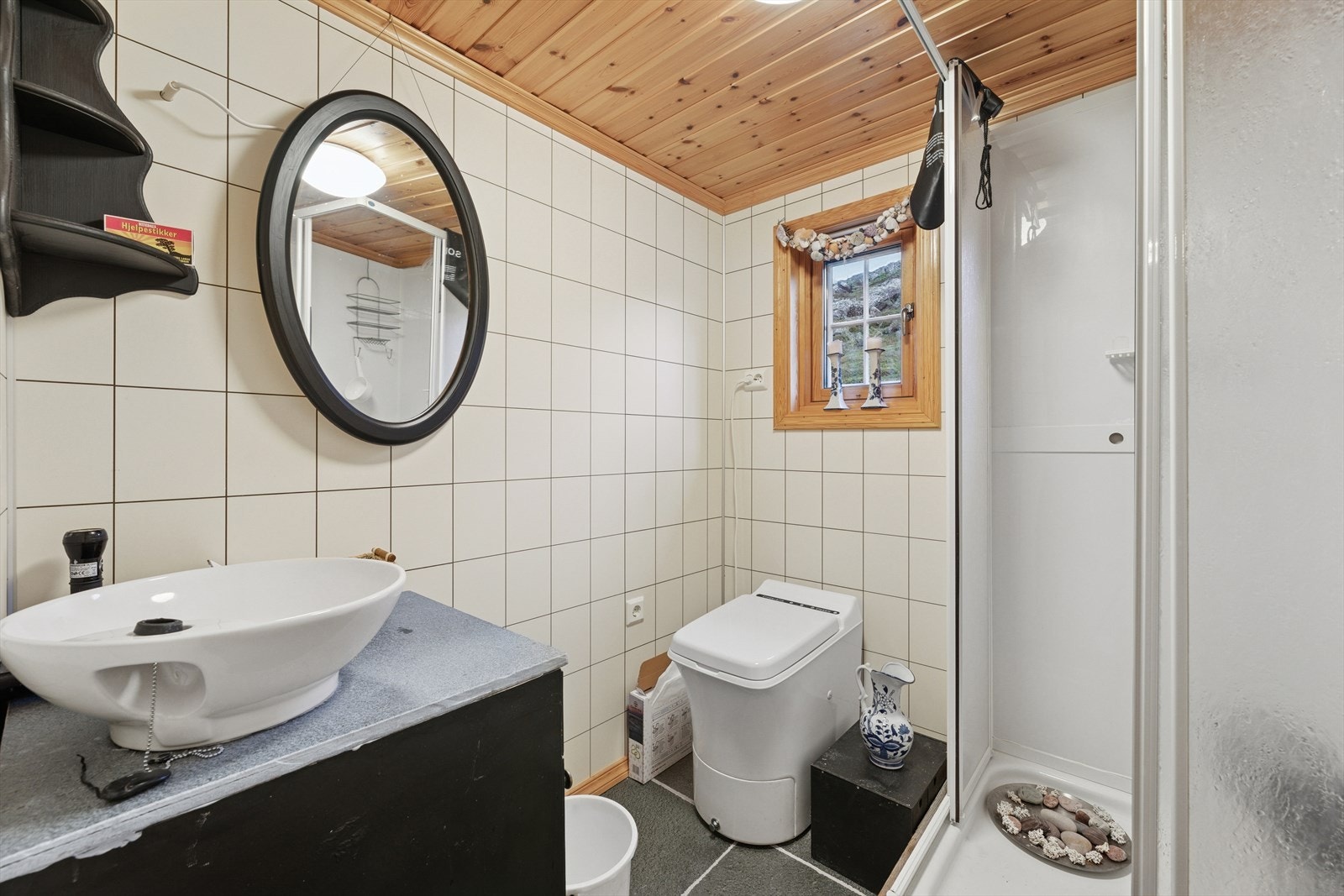 Toalettrom med skifer på gulv og våtromsplater på vegg. Rommet er utstyrt med forbrenningstoalett, dusjkabinett og enkel bolleservant. Galleribilde
