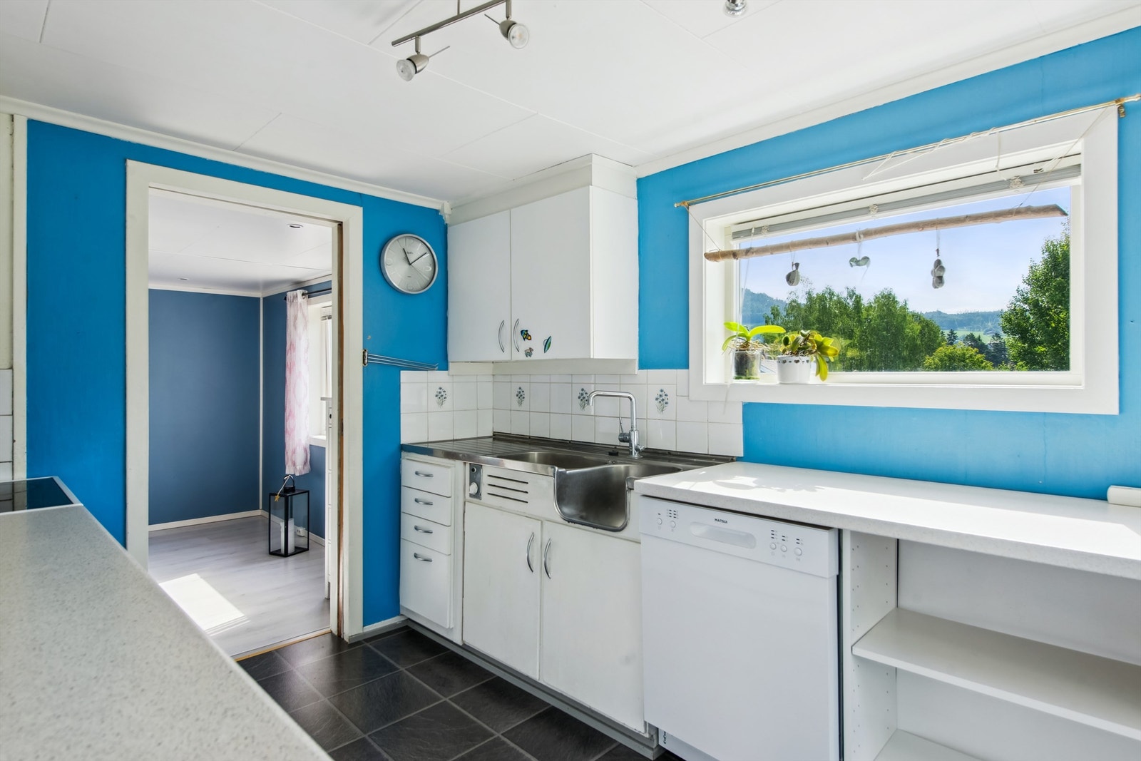 Kjøkkenet har avsatt plass til frittstående komfyr, kjøleskap og oppvaskmaskin. Innredningen bærer preg av generell slitasje. Galleribilde