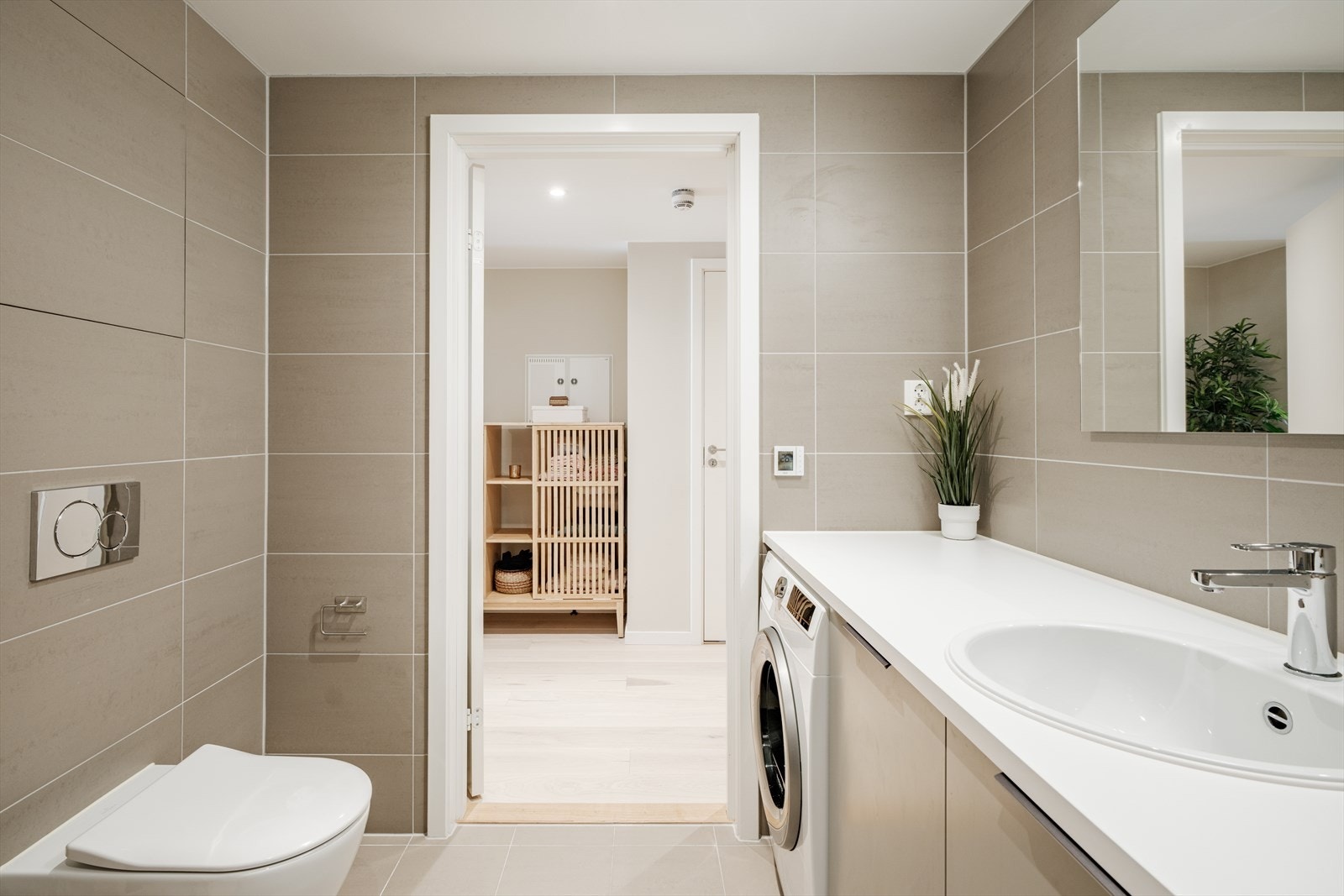 Leiligheten har et romslig, flislagt bad med vannbåren gulvvarme. Her finner du et stort dusjhjørne/nisje, vegghengt toalett og veggmontert servantinnredning. Galleribilde