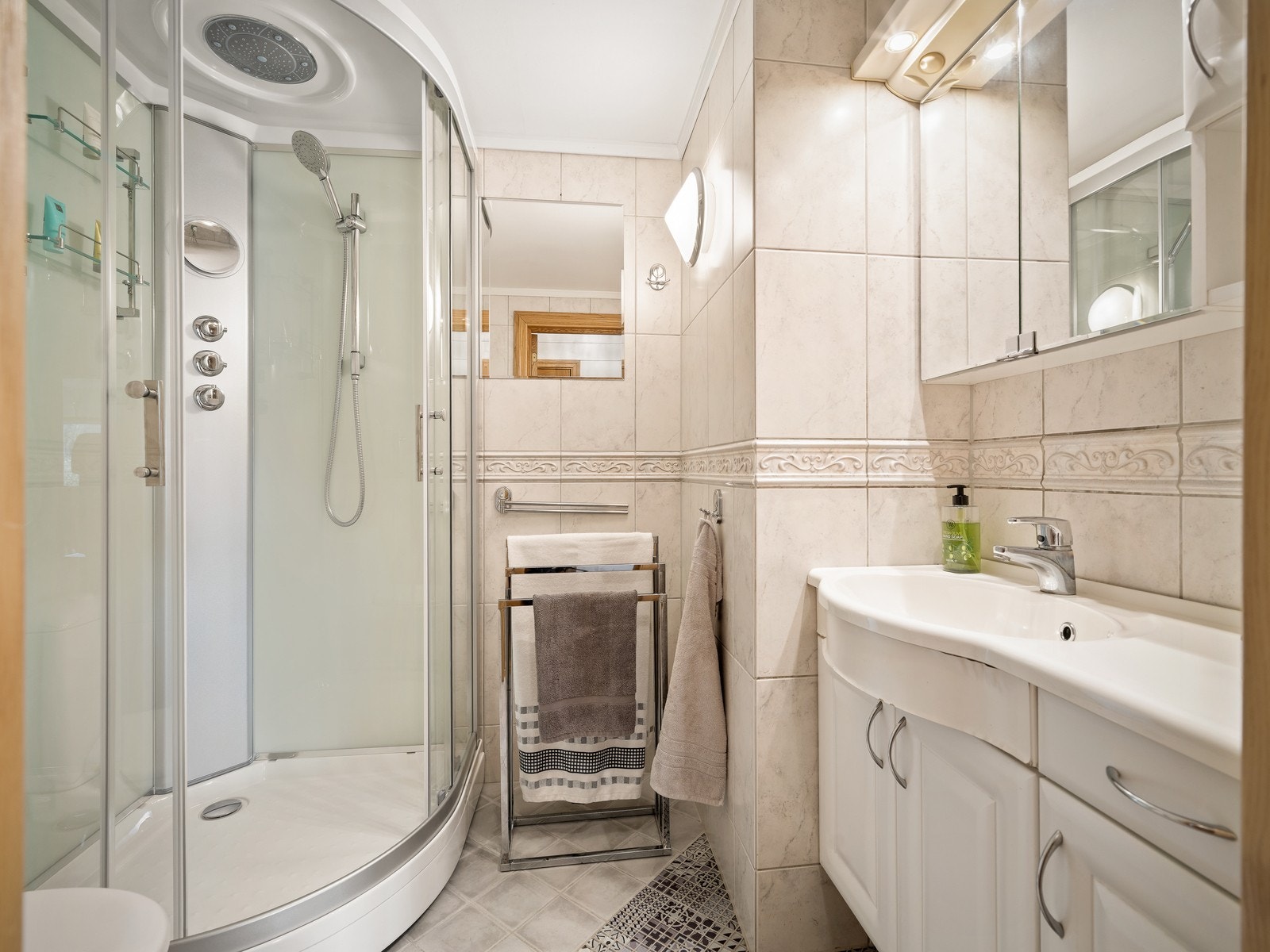 Badet har flislagte vegger og gulv og er innredet servant i skap, toalett og dusjkabinett. Det er elektriske varmekabler i gulvet. Galleribilde