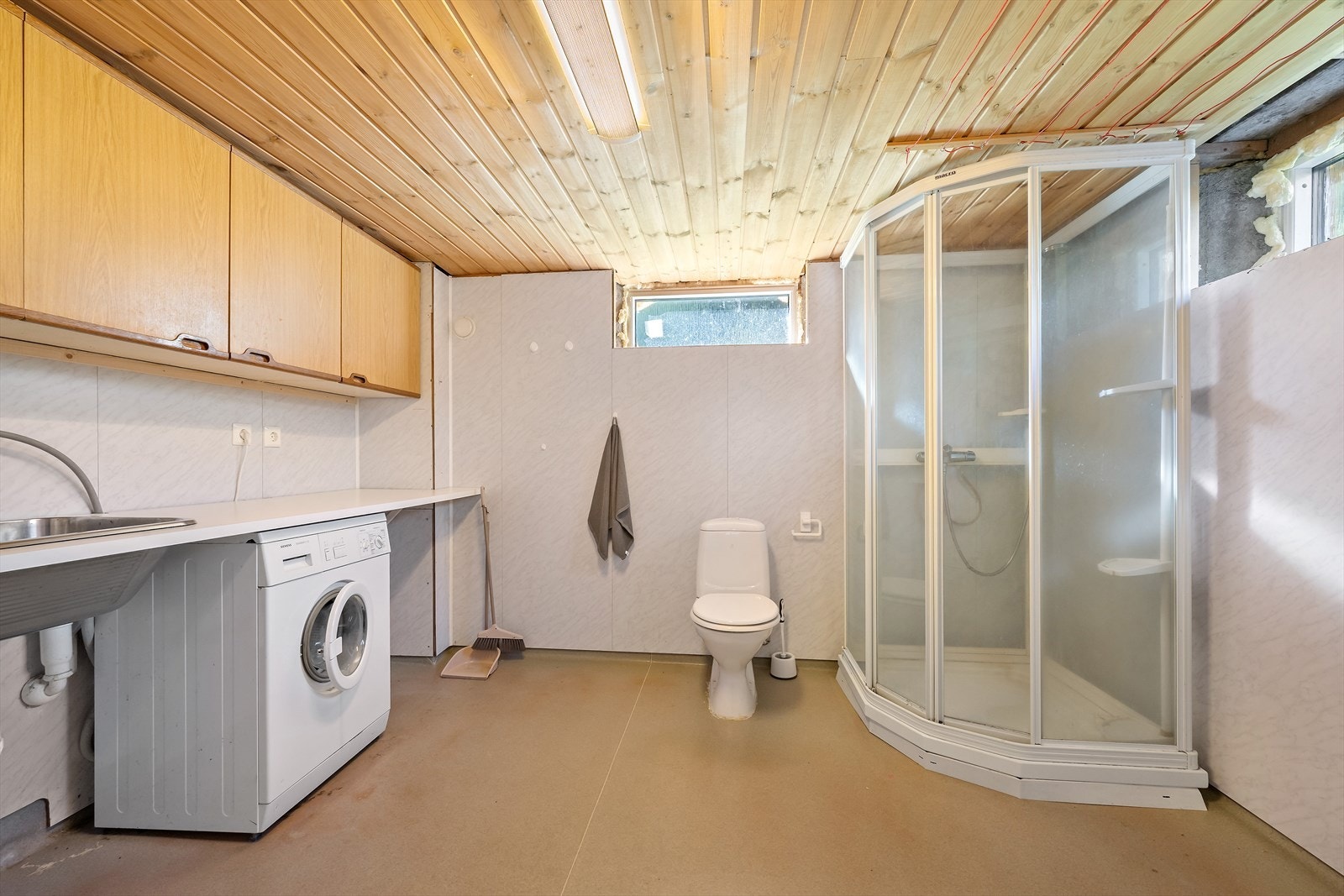 Bad/vaskerom i kjeller er innredet med toalett og dusj, samt benkeplate med nedfelt skyllekar, skap, og opplegg for vaskemaskin. Galleribilde