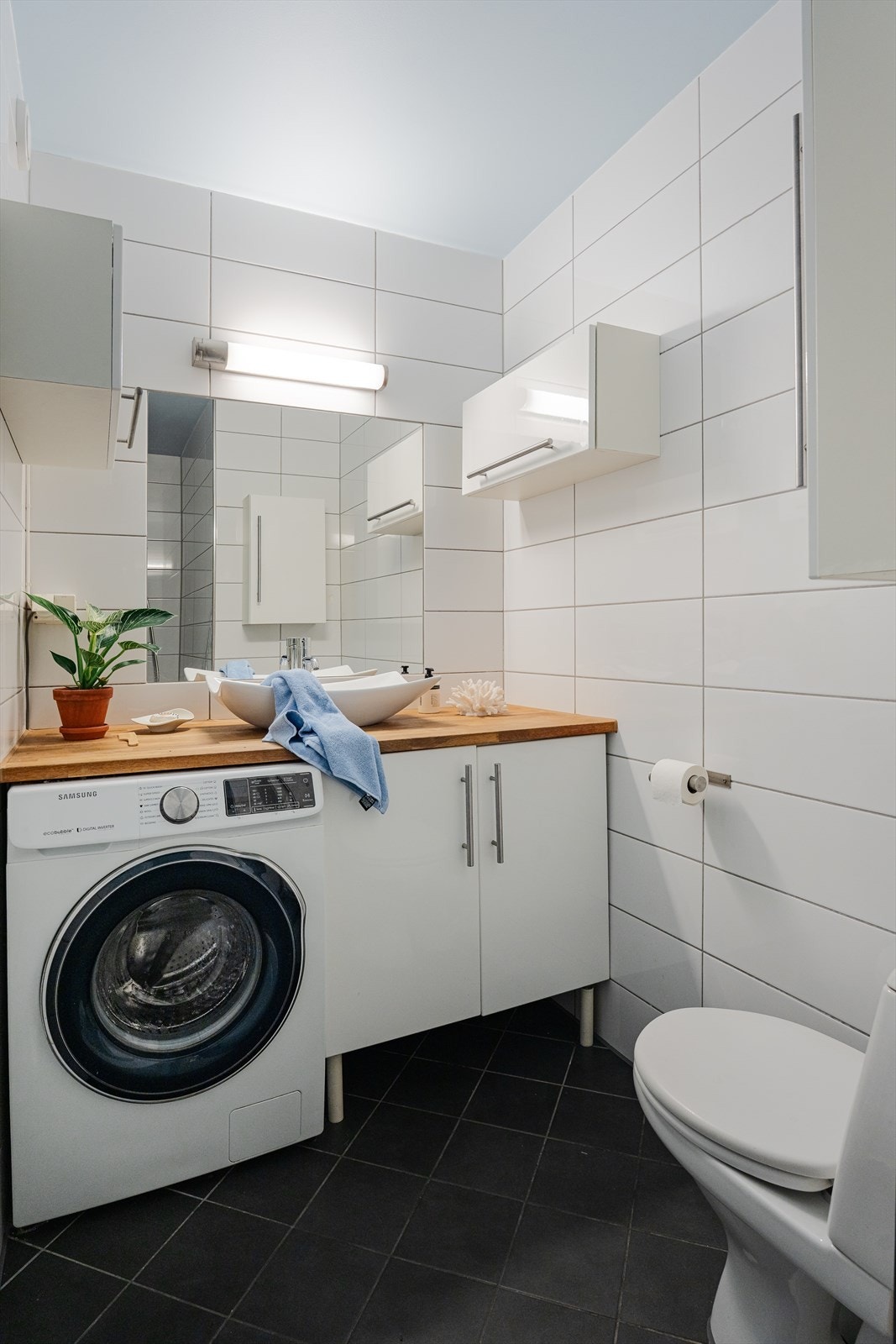 Lyst helfliset baderom utstyrt med wc, servantskap og opplegg for oppvaskmaskin. Gulvvarme Galleribilde