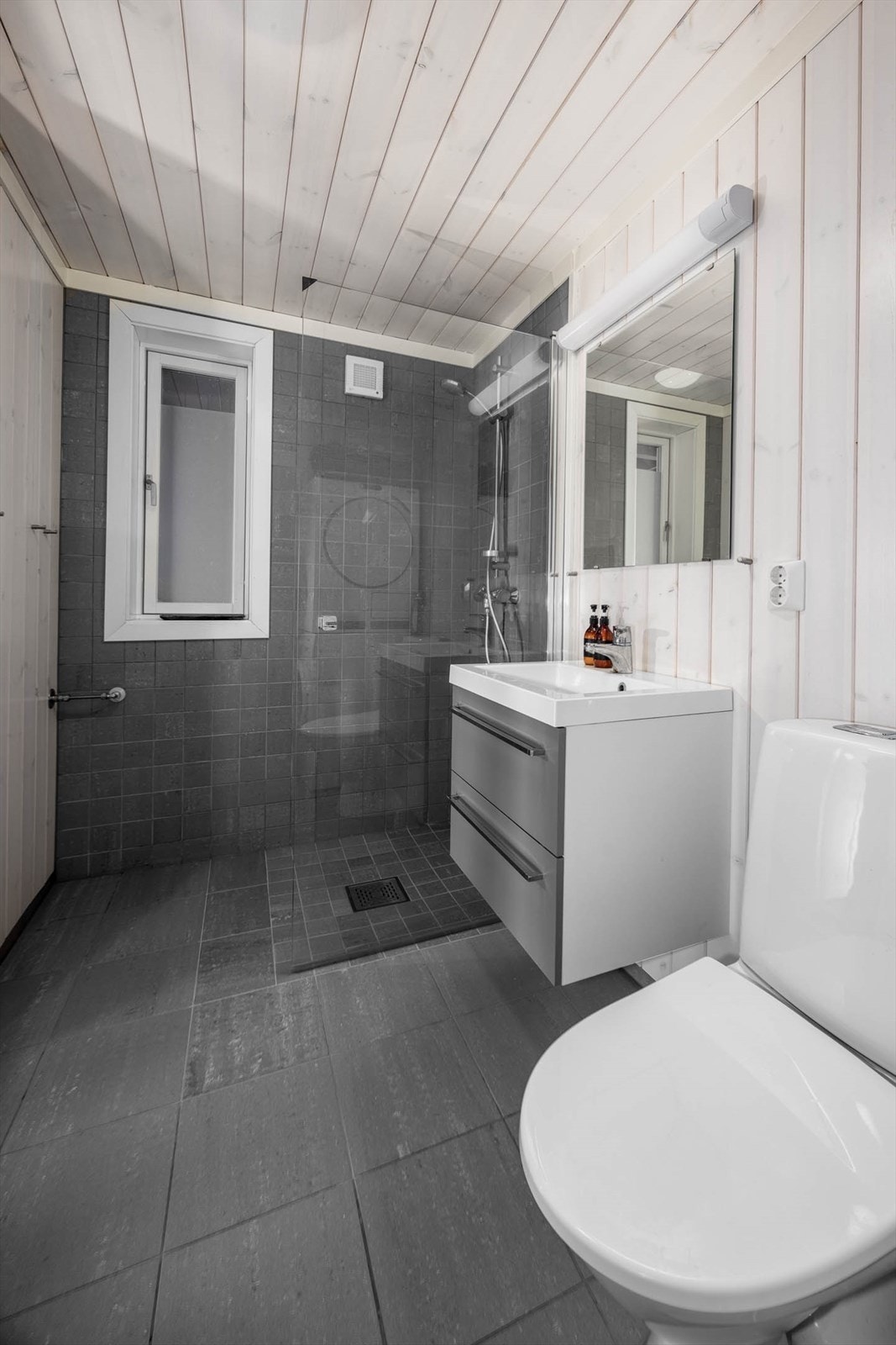 Baderom i tidsmessige gråtoner og panelte vegger og tak. Galleribilde