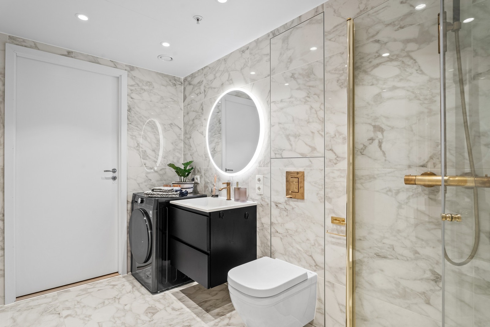 Dusjsone med svingdører i glass og regnfallsdusj, håndkletørker på veggen og opplegg for vaskemaskin. Downlights i himlingen gir godt lys. Galleribilde