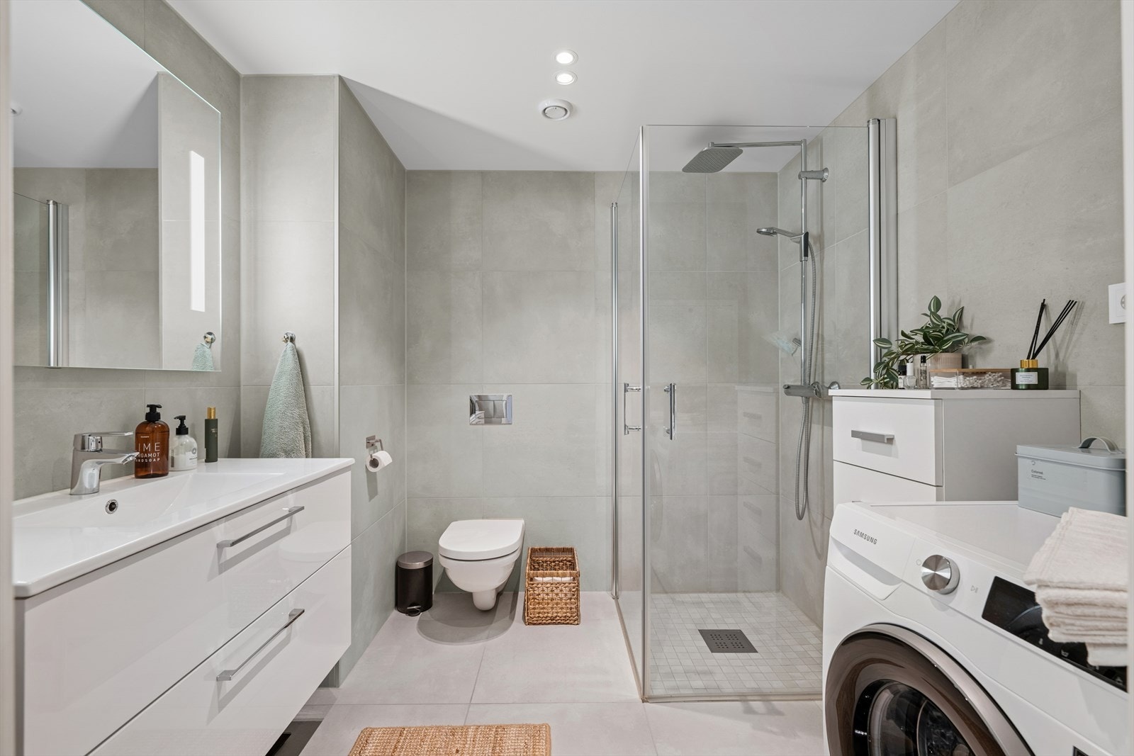 Badet har flislagte vegger og gulv med elektriske varmekabler som gir god komfort. Himlingen er malt, og rommet er utstyrt med moderne innredning med nedfelt servant, vegghengt toalett og dusjhjørne med glassvegger. Galleribilde