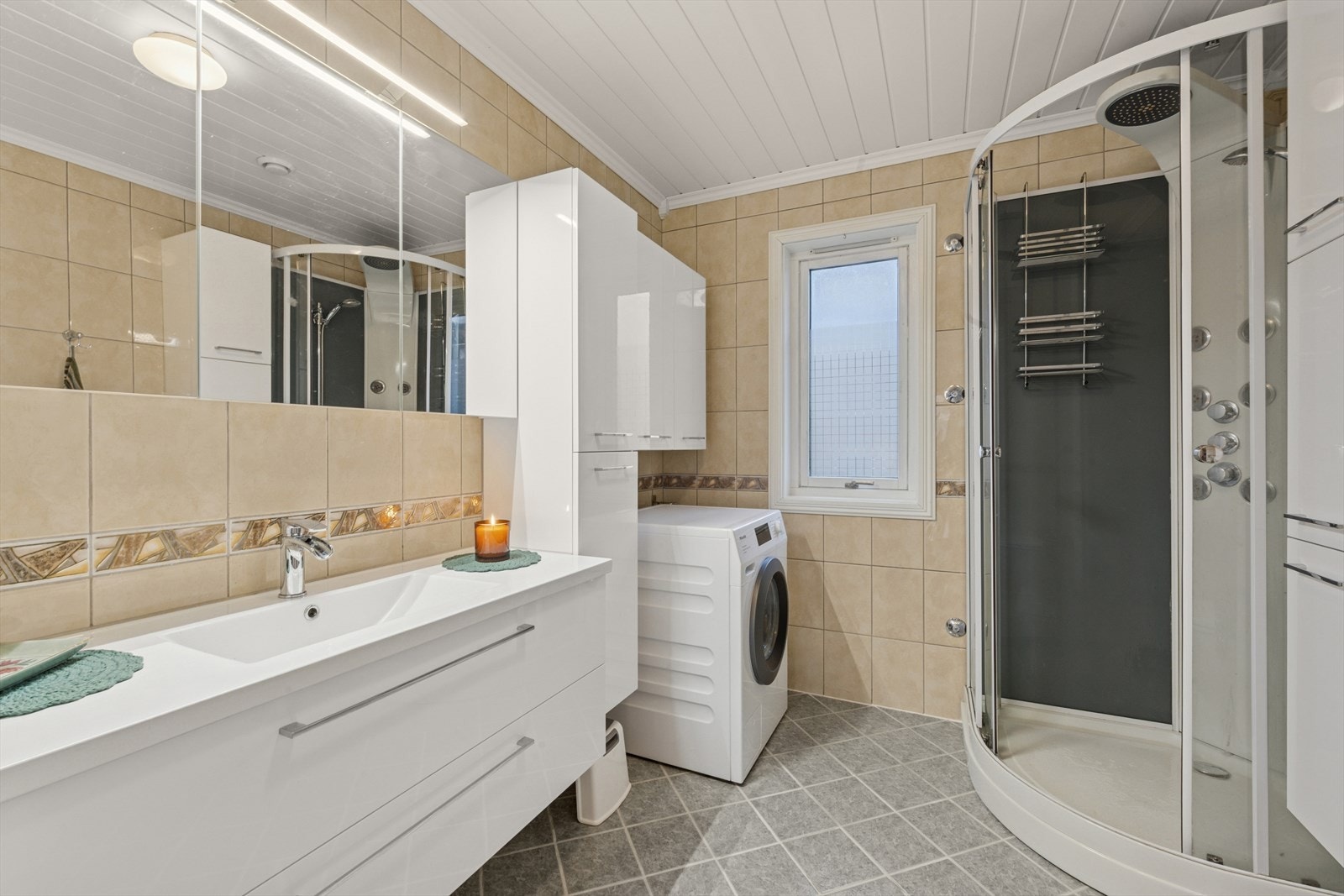 Pent flislagt bad utstyrt med dusjkabinett, lys og moderne baderomsinnredning, opplegg for vaskemaskin og gulvstående toalett. Galleribilde