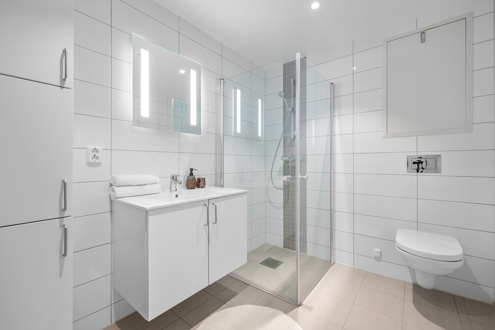 Stilrent og flislagt bad på 5,3 kvm. Inneholder vegghengt wc, dusjhjørne, servant med speil, oppbevaringsskap og opplegg for vaskemaskin. Galleribilde