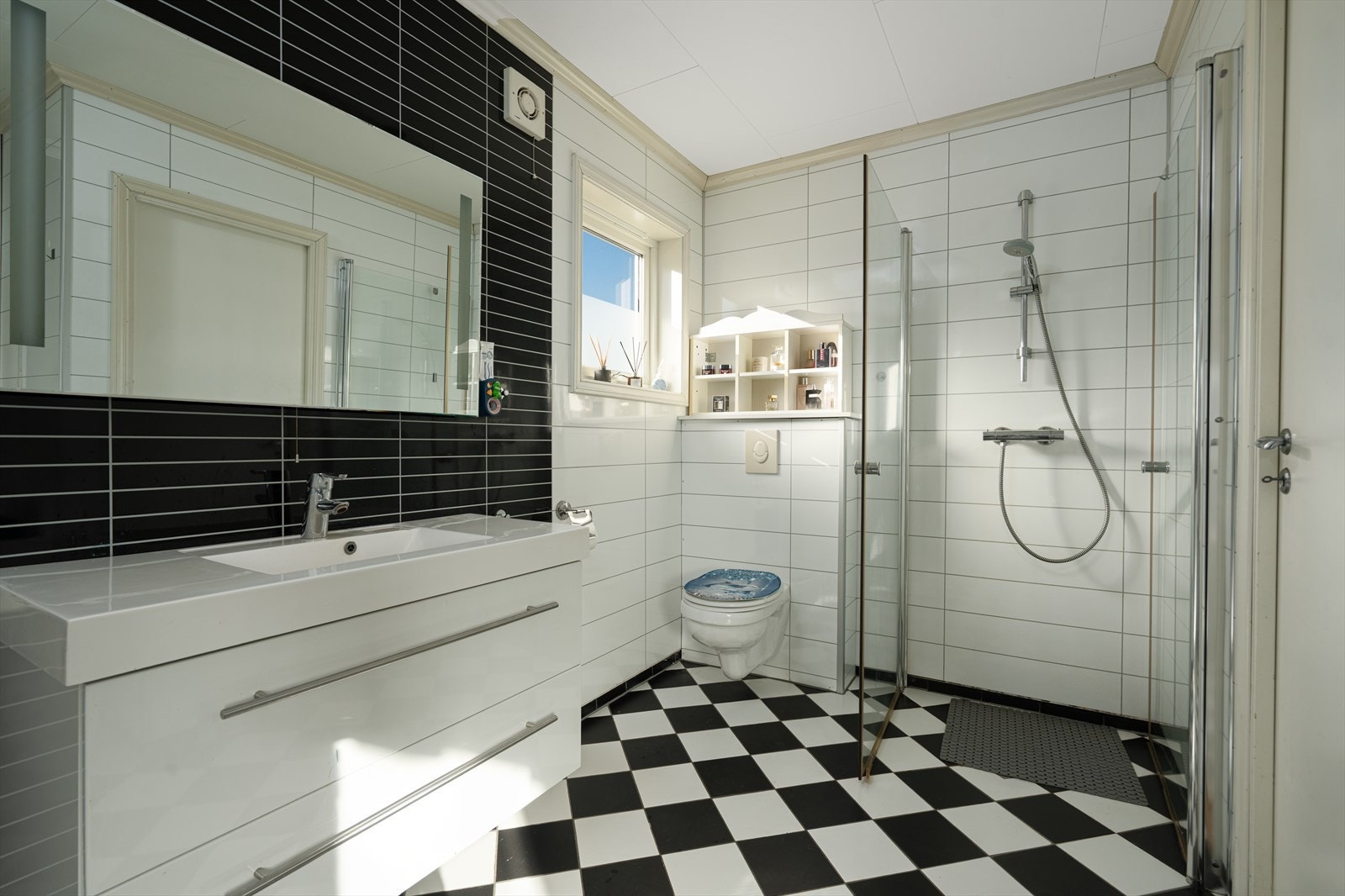 Pent og romslig bad med fliser på gulv og våtromspanel på vegg. Rommet inneholder seksjon med servant, dusjhjørne med svingbare glassdører, badekar og toalett. Galleribilde