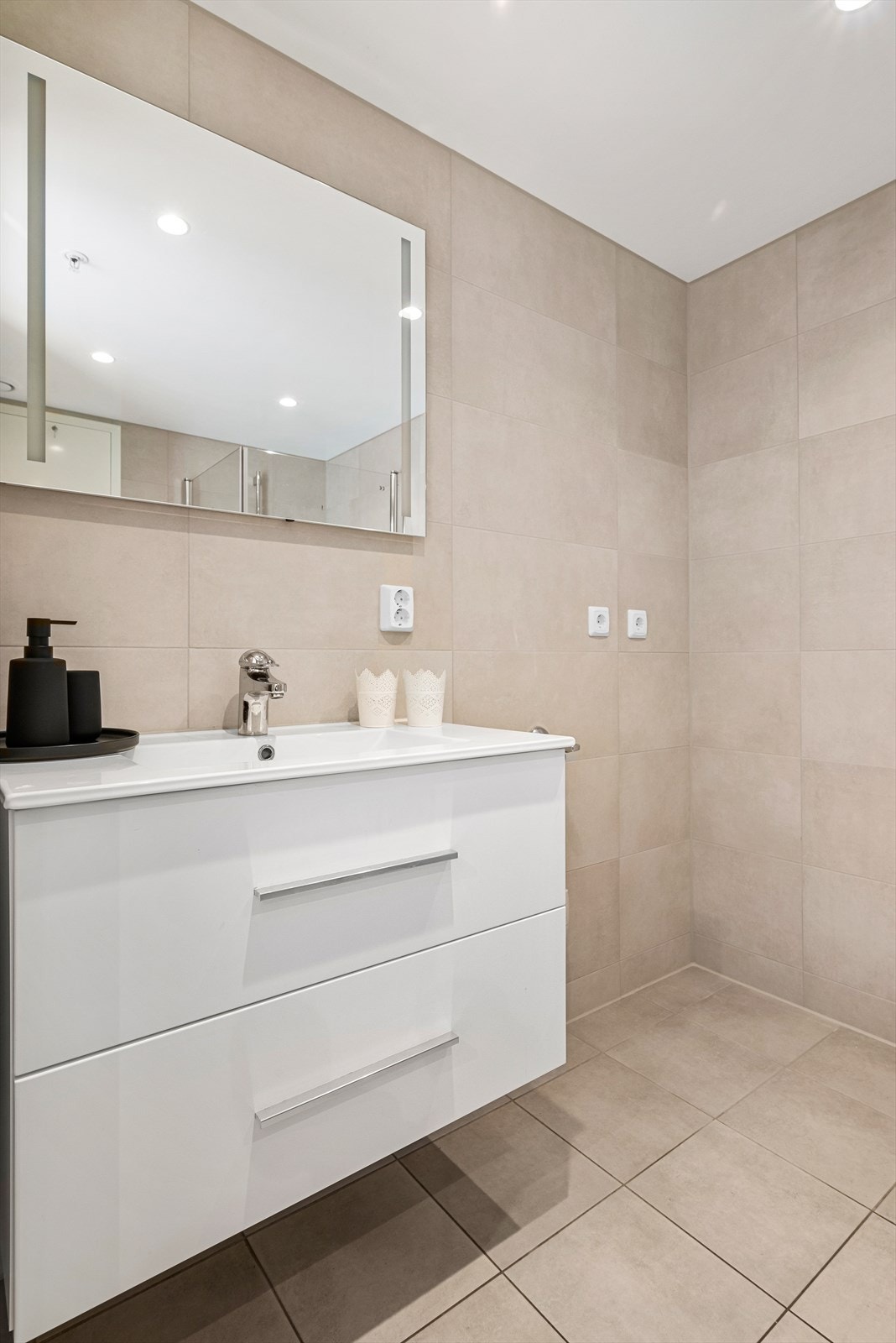 Baderomsinnredningen har heldekkende servant med skuffer under og vegghengt speil med integrert belysning. Innenfor innredningen er det plass til vaskerom og tørketrommel. Galleribilde