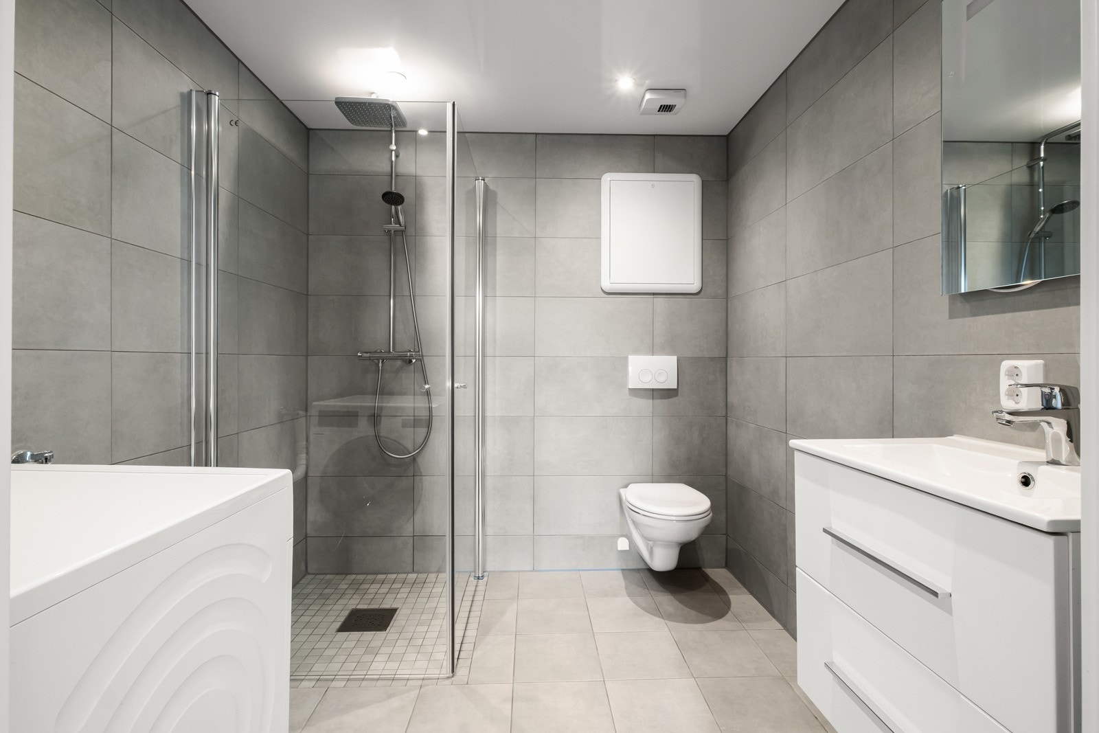 Hovedbadet er utstyrt med veggmontert toalett, servant med skuffer og speil, dusj med glassvegg og opplegg for vaskemaskin. Galleribilde