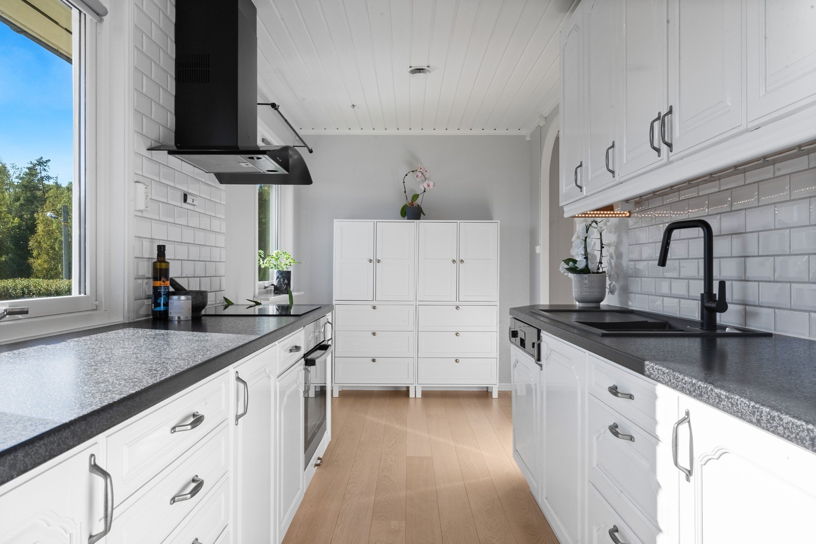 Kjøkken fra 2015 med moderne uttrykk og svarte detaljer. Det er plass til spisebord ved kjøkkenvindu i enden av kjøkkenet. Galleribilde