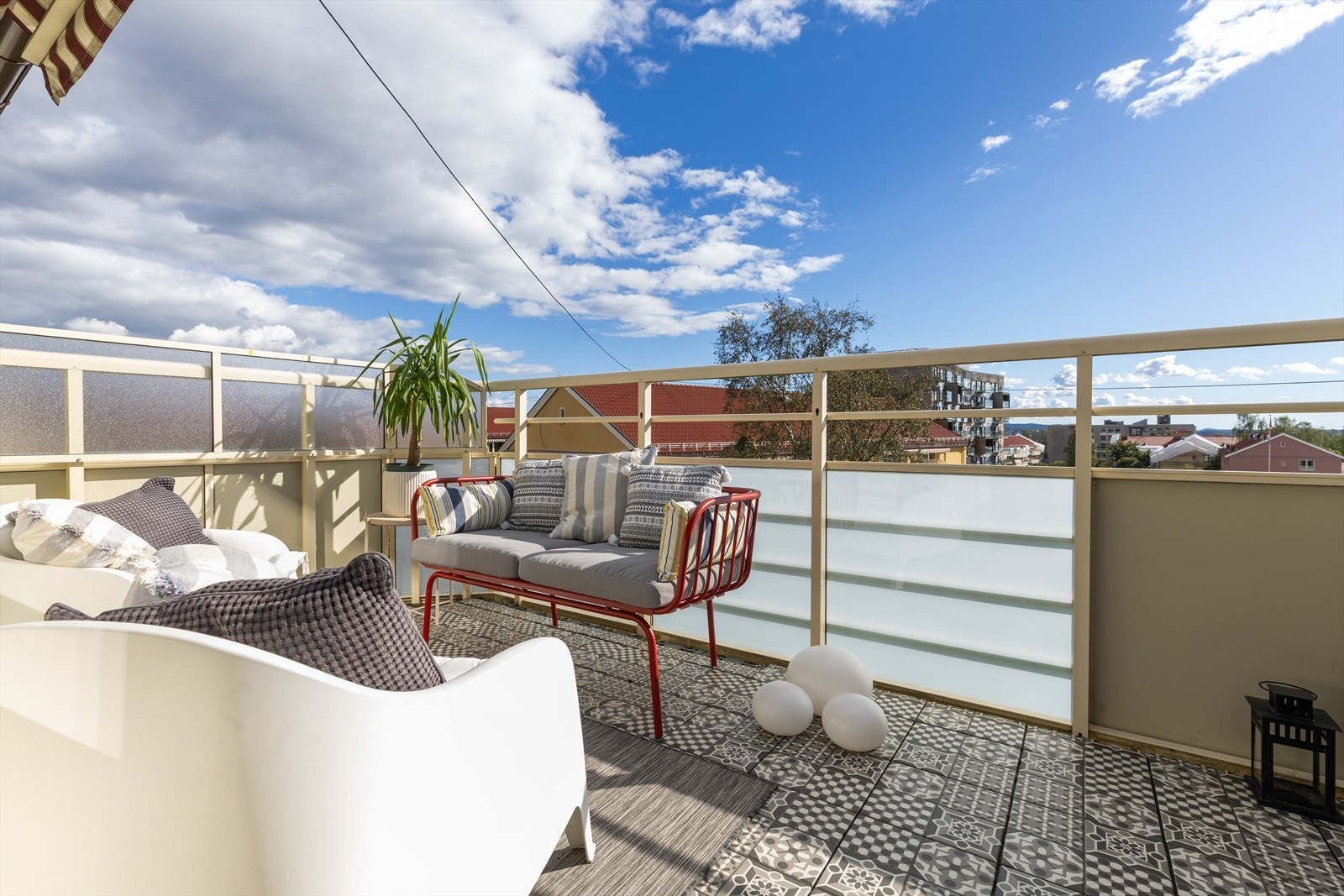 Balkongen vender mot sør og har flisheller på gulvet. Den er utstyrt med strømuttak, lysarmatur og en motorisert markise montert på veggen - praktiske detaljer som gjør uteplassen både komfortabel og funksjonell. Galleribilde