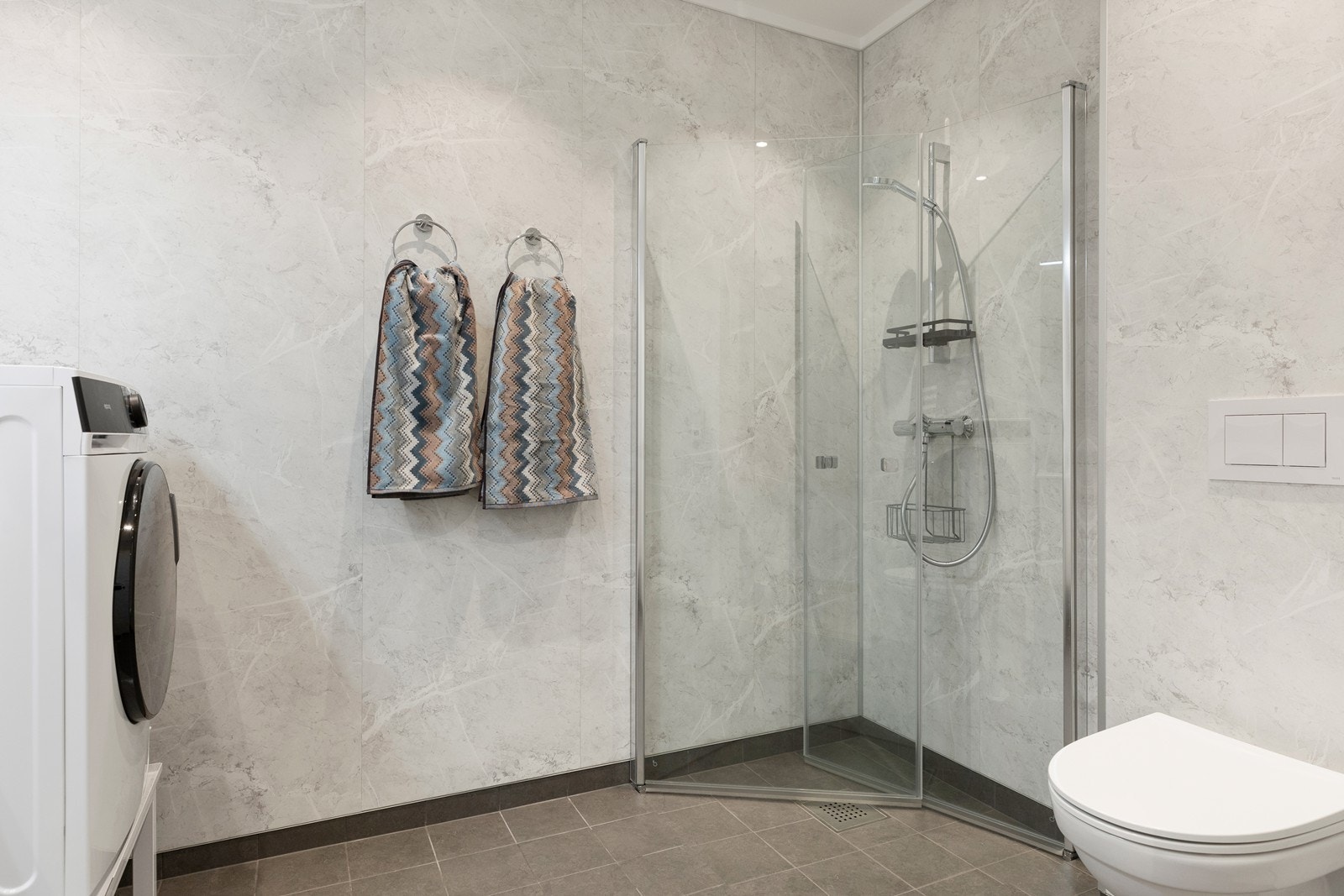 Badet inneholder videre vegghengt toalett, som gjør det enkelt å holde badet rent, samt dusjløsning med glassvegger som kan skyves inn. Galleribilde