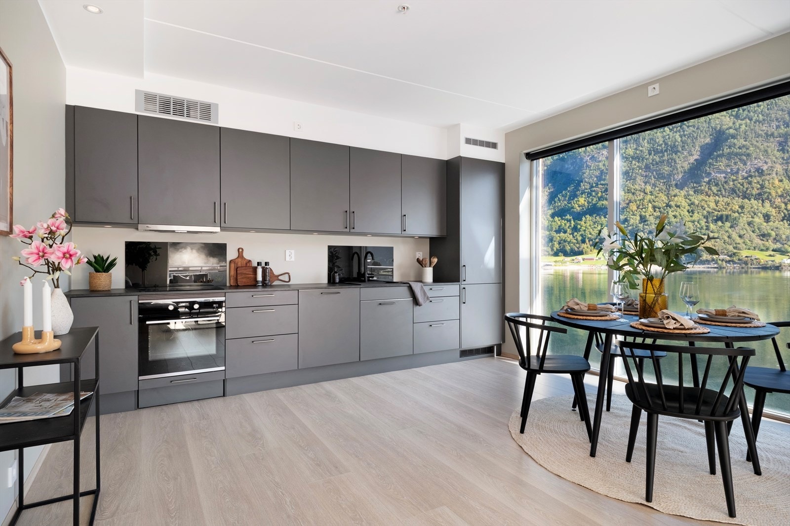 Kjøkkendelen har stilfull innreiing med mørke glatte frontar og veggbeskyttelse bak platetopp og vask. Galleribilde