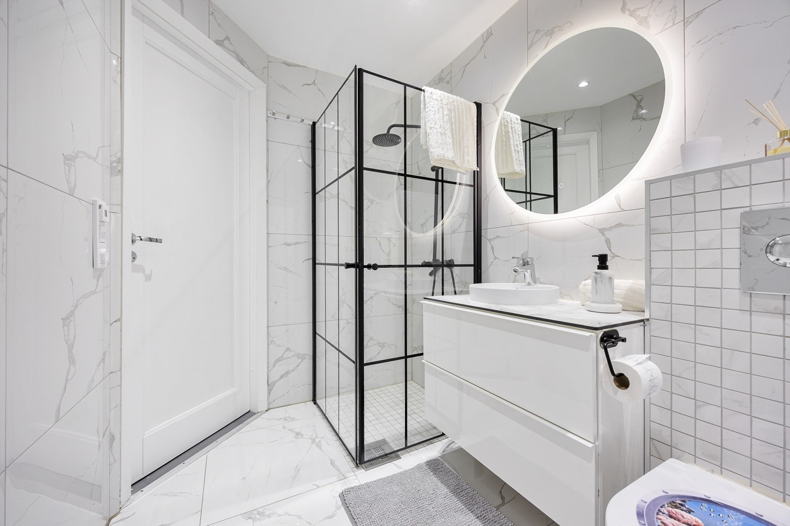 Baderommet består av dusjløsning, servantseksjon med skuffer, speil med integrerte lys, vegghengt klosett og opplegg for vaskemaskin. Galleribilde