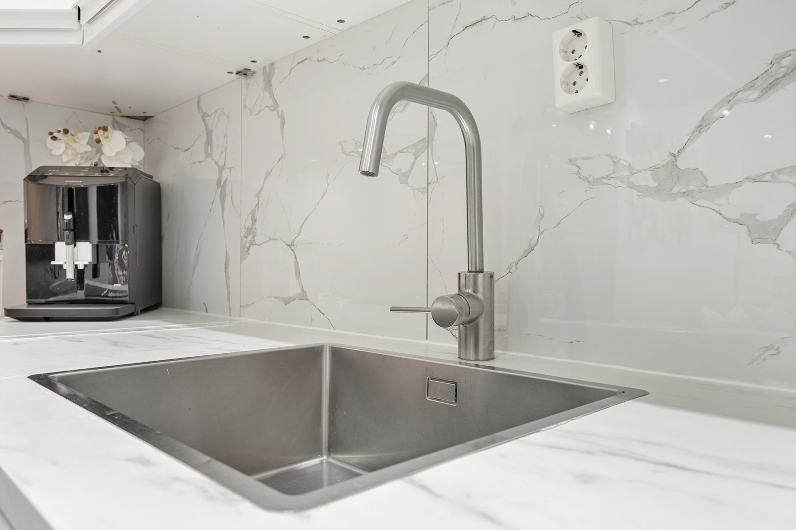 Moderne marmor-design på vegg over benkeplate gir kjøkkenet et stilrent utrykk. Galleribilde