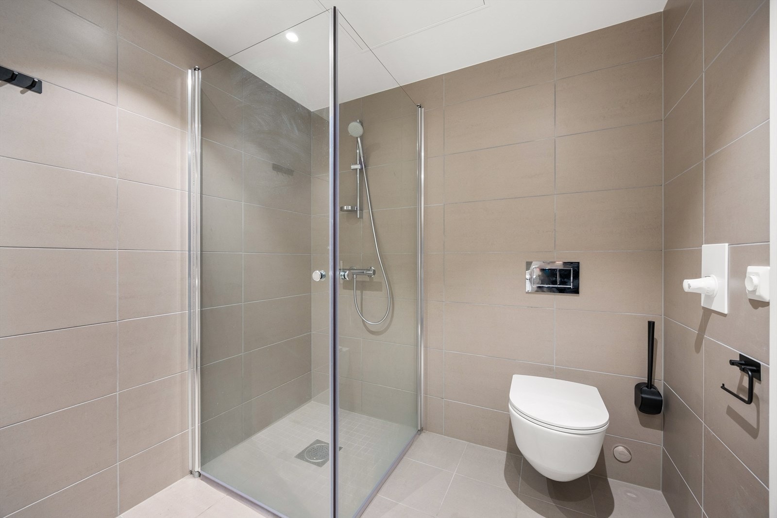 Badet består av servantseksjon med skuffer, dusjhjørne, vegghengt klosett, speil og opplegg for vaskemaskin. Galleribilde