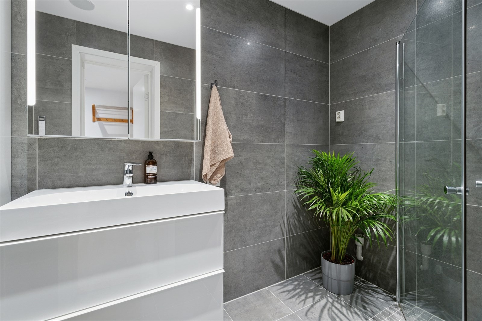 Baderommet er ca. 4 m² og har flis på gulv og vegg, malt slett himling. Badet har en flott skuffinnredning med servant og lyssatt speil over, dusjnisje samt opplegg for vaskemaskin. Galleribilde