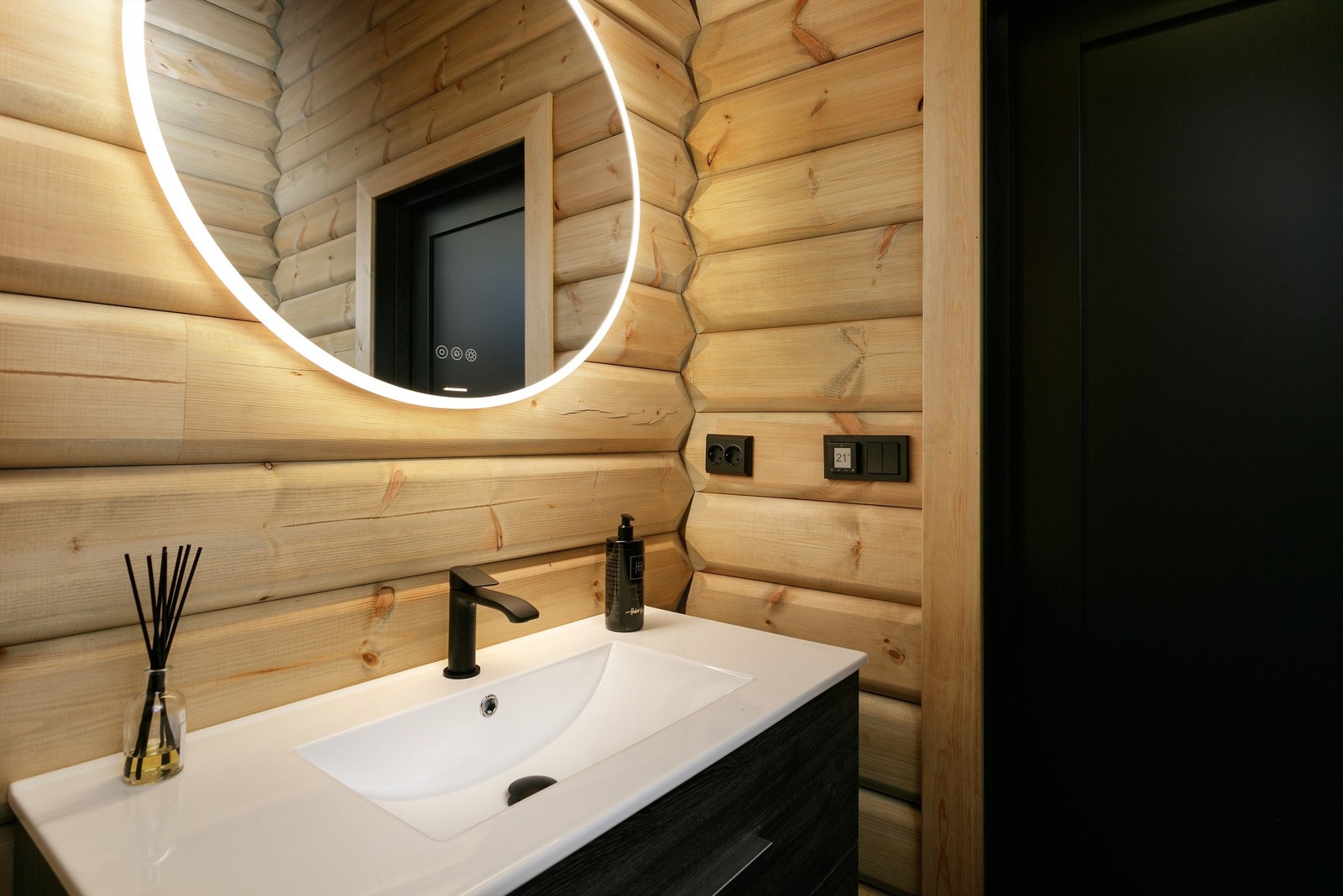 Sort baderomsinnrending med skuffer og ovenpåliggende servant med sort ett-greps armatur. Speil med lys og stikkontakter over servant. Galleribilde