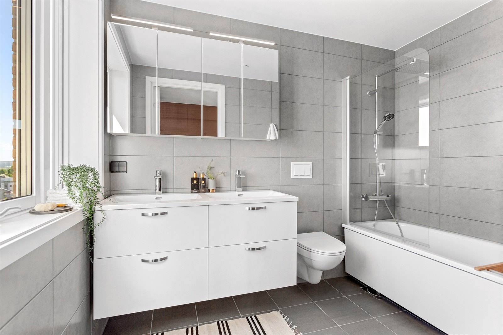 Delikat bad med dobbel servant, speilskap med overlys, vegghengt toalett og badekar med dusj. Galleribilde