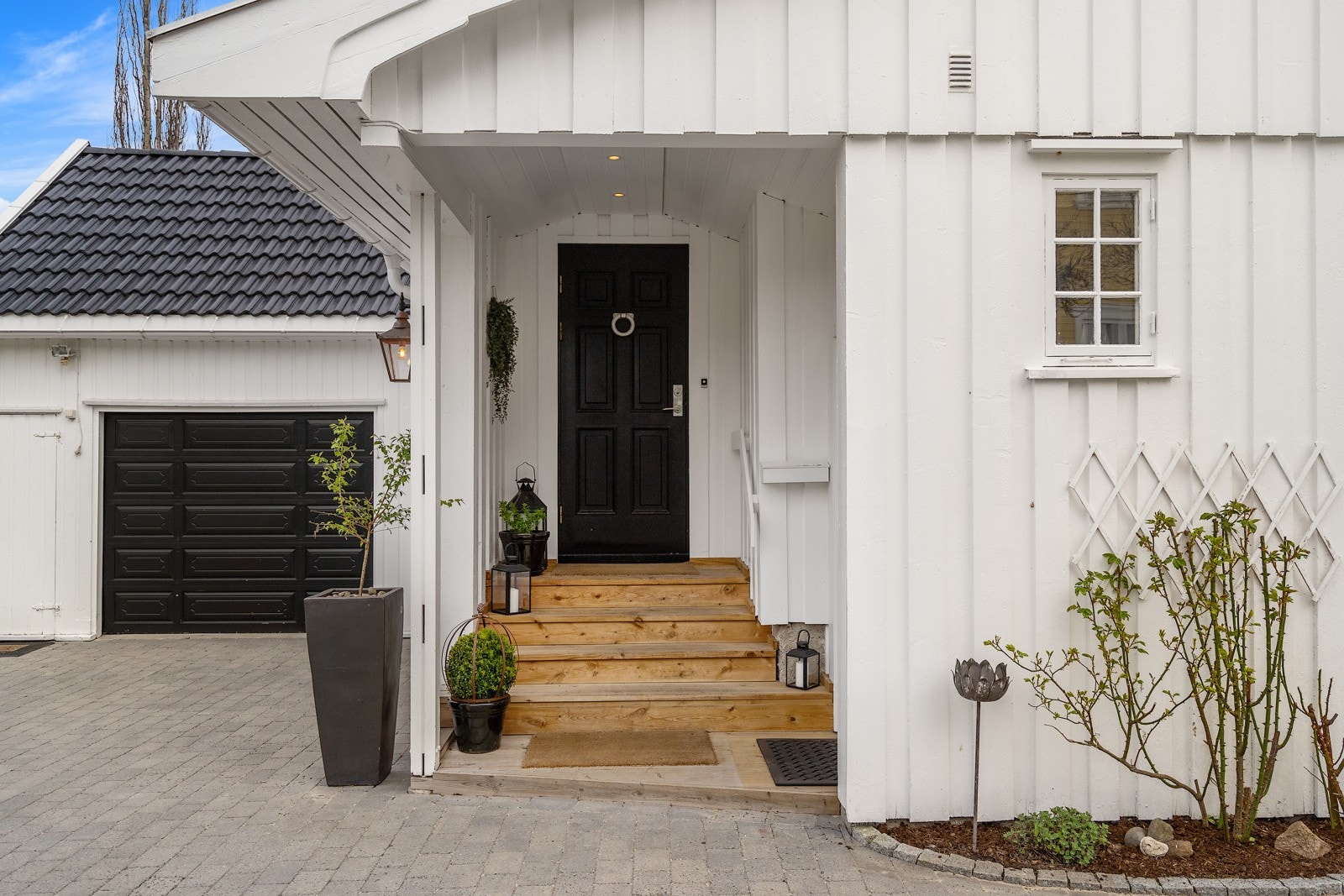 Inngangen er overbygd og godt skjermet, med ringeklokke, sort ytterdør og tretrapp av nyere dato Galleribilde