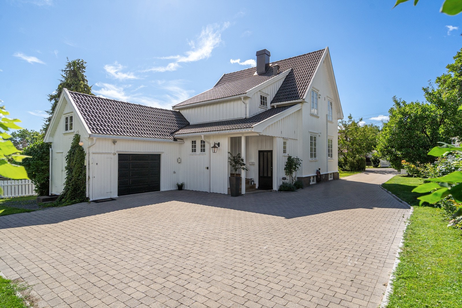 En innkjørsel med belegningsstein glir over i et stort gårdsrom på inngangssiden, med garasje, utekran og 2 ladere for elbil montert i senere tid. Garasjen har to tilbygde boder og et samlet areal på ca. 29 kvm. Galleribilde